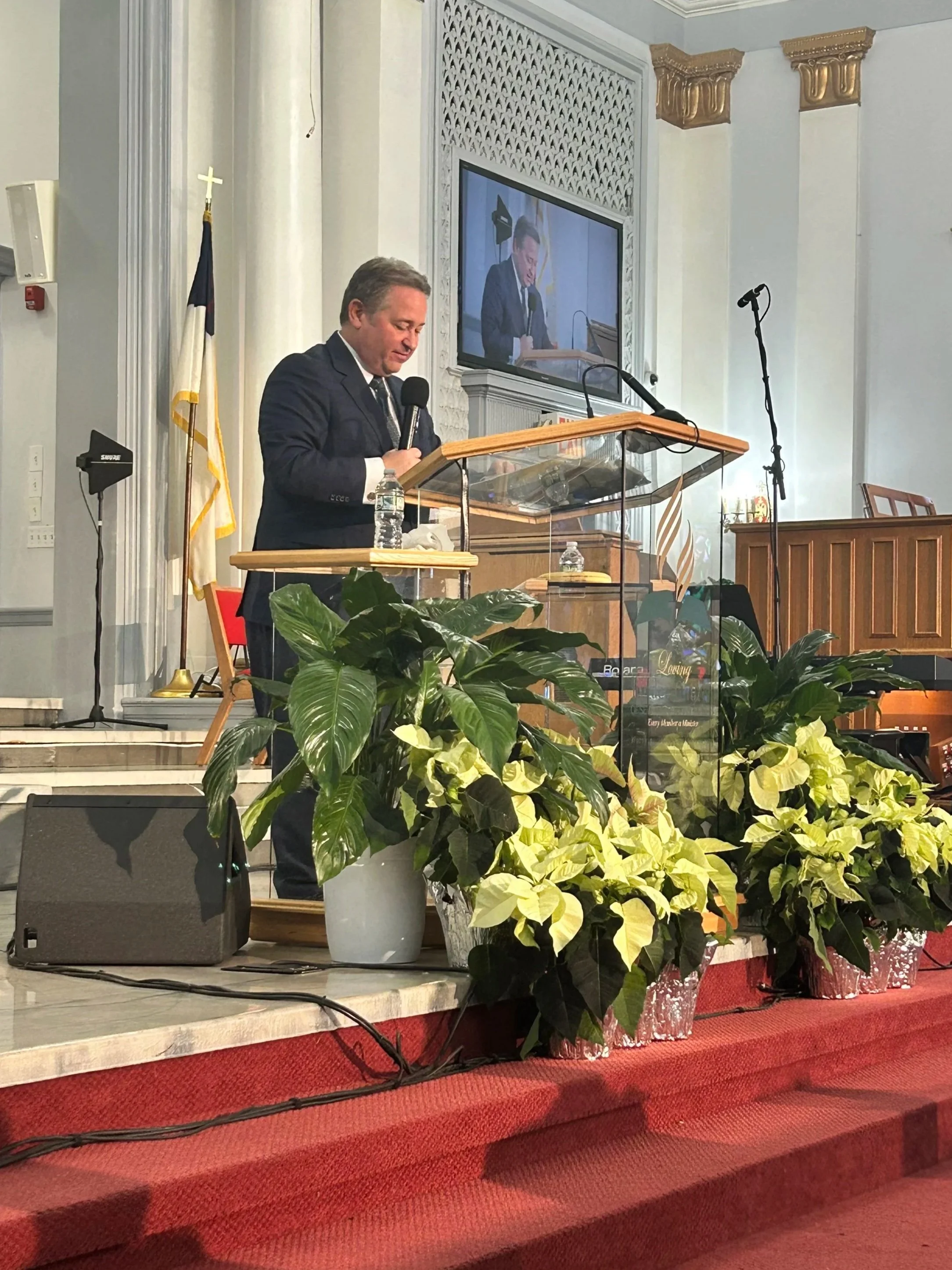 A pastor stands at the altar in a nice modern church leading prayer. Board and Leadership Development.