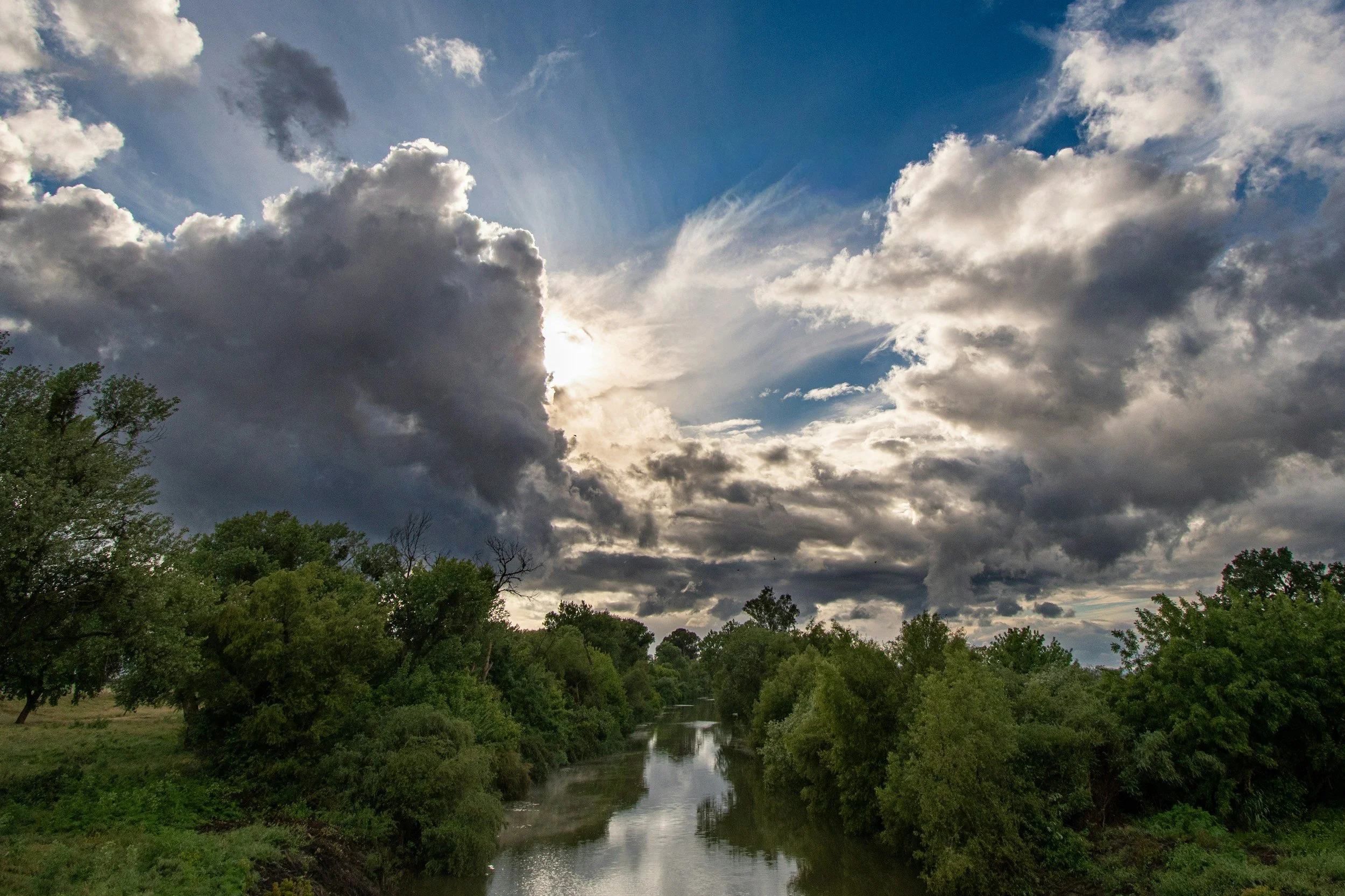 Cloudy sky over a river surrounded by green trees and grass.