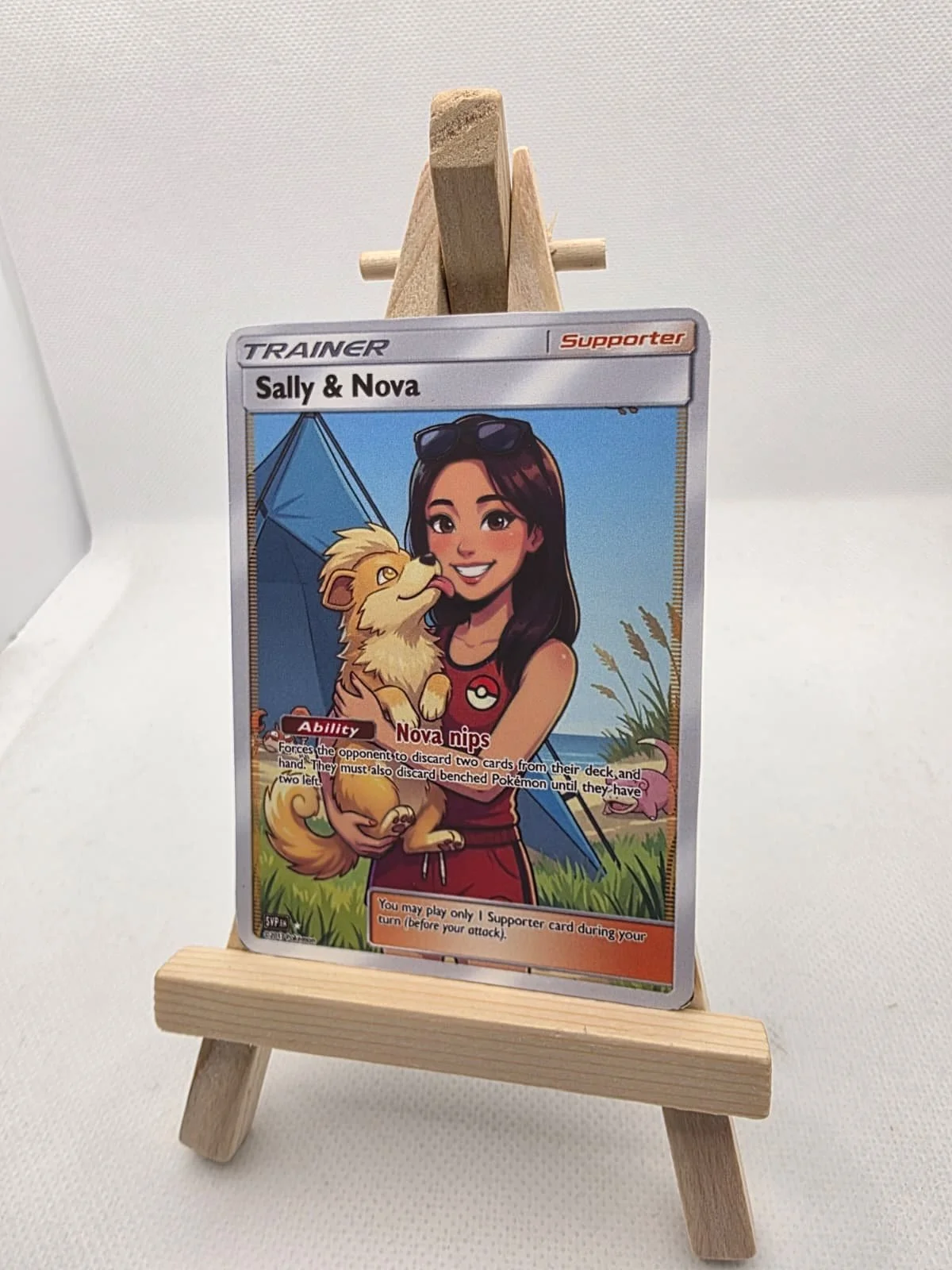 A Pokémon Trainer card featuring Sally & Nova, with an illustrated woman holding a small dog in front of a camping scene with a tent and pink flamingos.  Aussie Custom Cards specializes in high-quality custom Pokémon cards and personalised trading ca