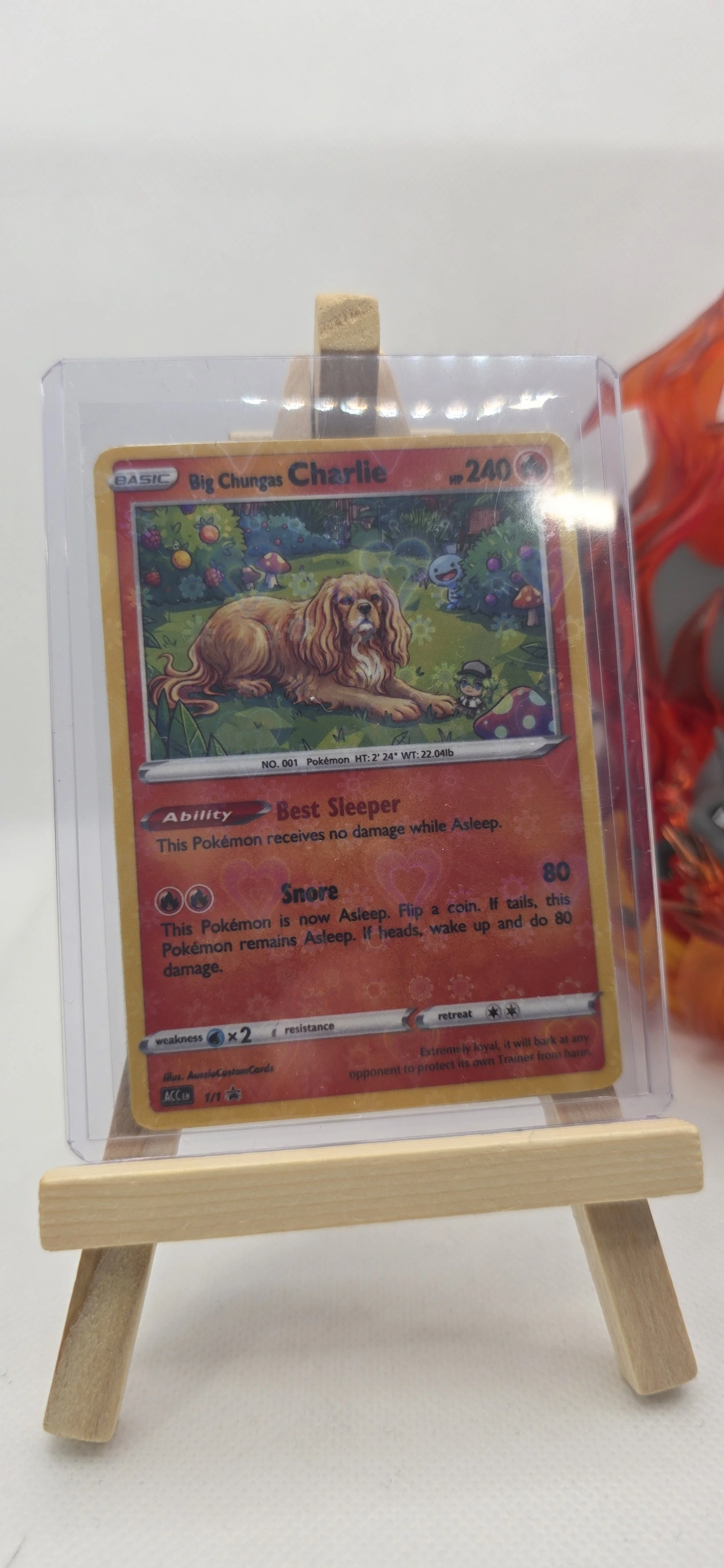 A Pokémon card for Big Chungas Charlie, a large dog with ability Best Sleeper and attack Snore, resting on small wooden easel with a white background.