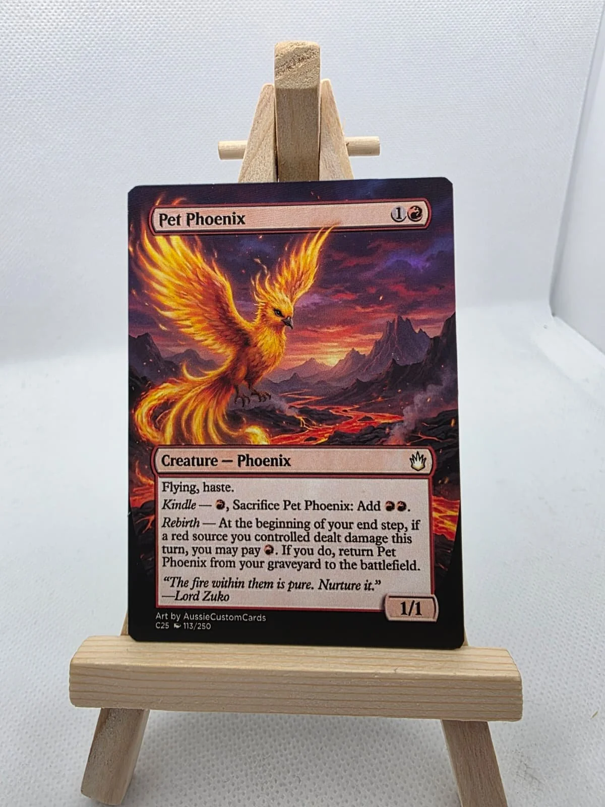 A fantasy trading card titled Pet Phoenix, depicting a fiery phoenix with large golden wings flying over a volcanic landscape at sunset.