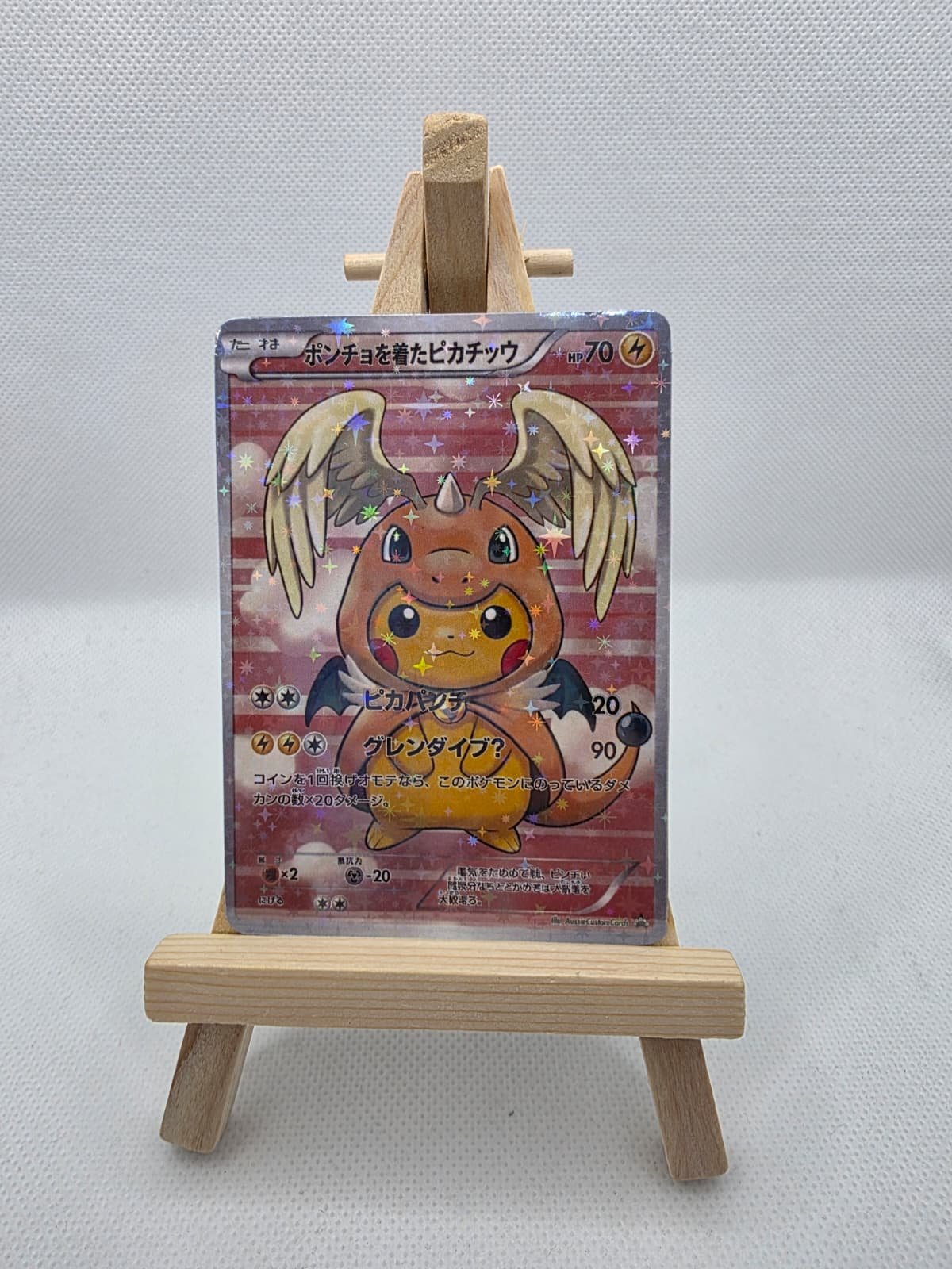 A Pokémon card depicting a cute, cartoonish creature with wings, horns, and a small body, displayed on a small wooden easel against a plain white background.