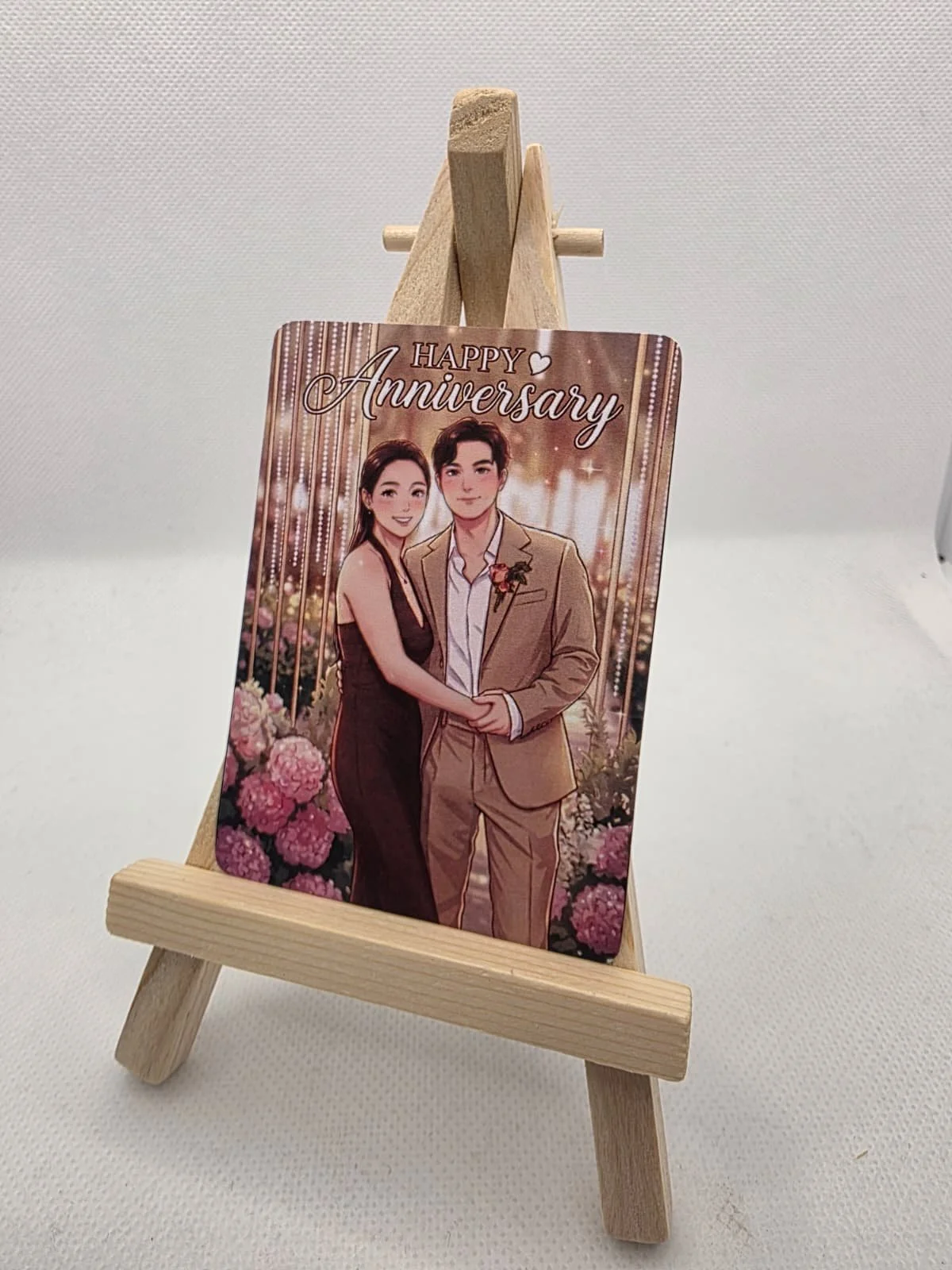 Anniversary card with an illustration of a couple holding hands, surrounded by pink flowers and hanging lights.