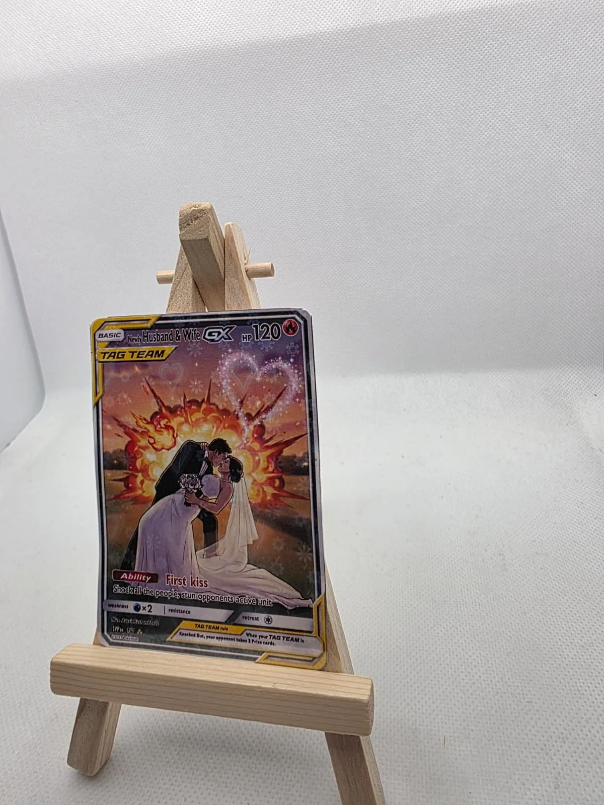 A Pokémon trading card featuring a wedding scene, titled 'Newly Husband & Wife,' displayed on a small wooden easel against a plain white background.