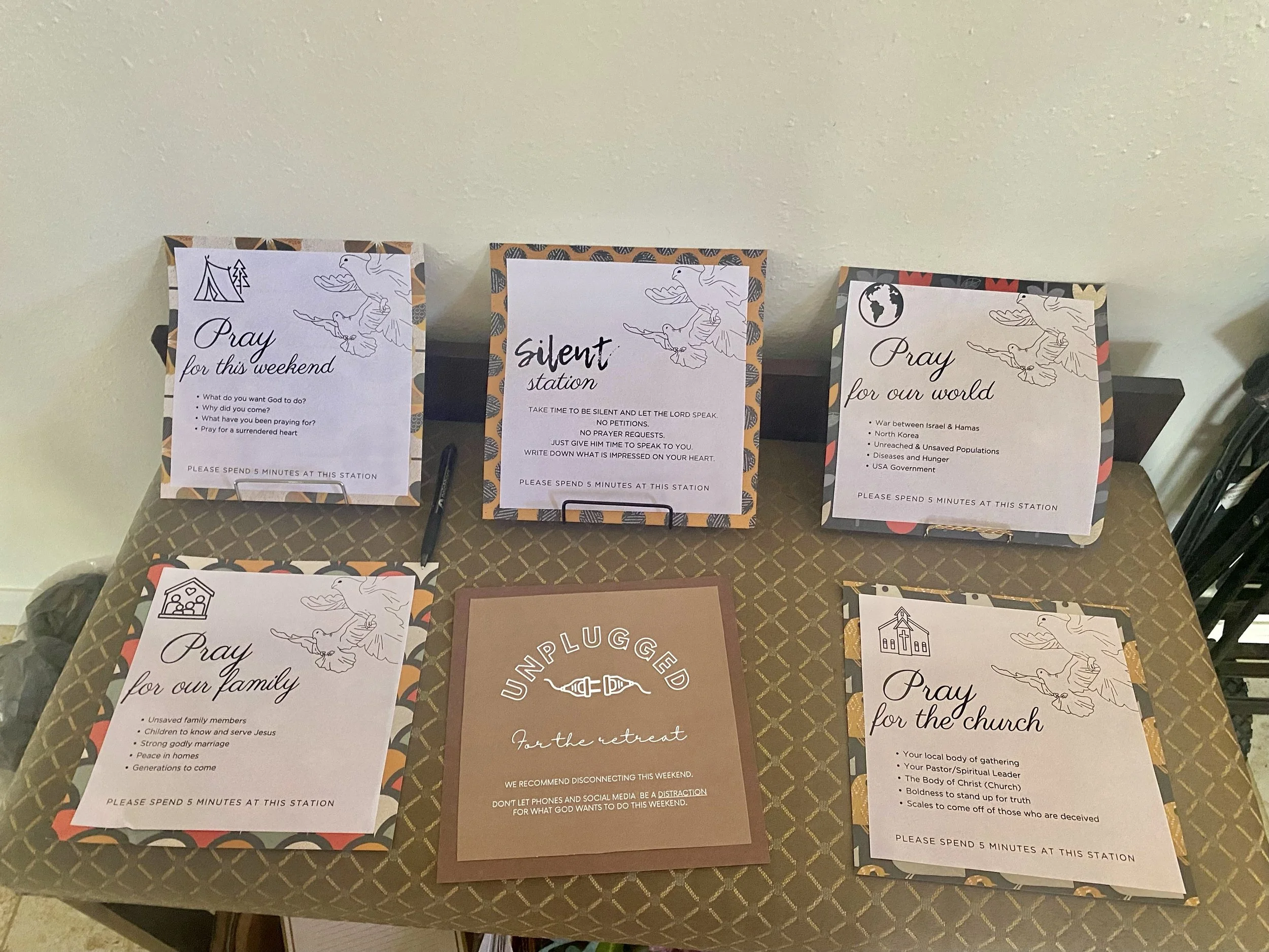 Table with four sign-up sheets for prayer themes, a sign about unplugging for the retreat, and a pen.