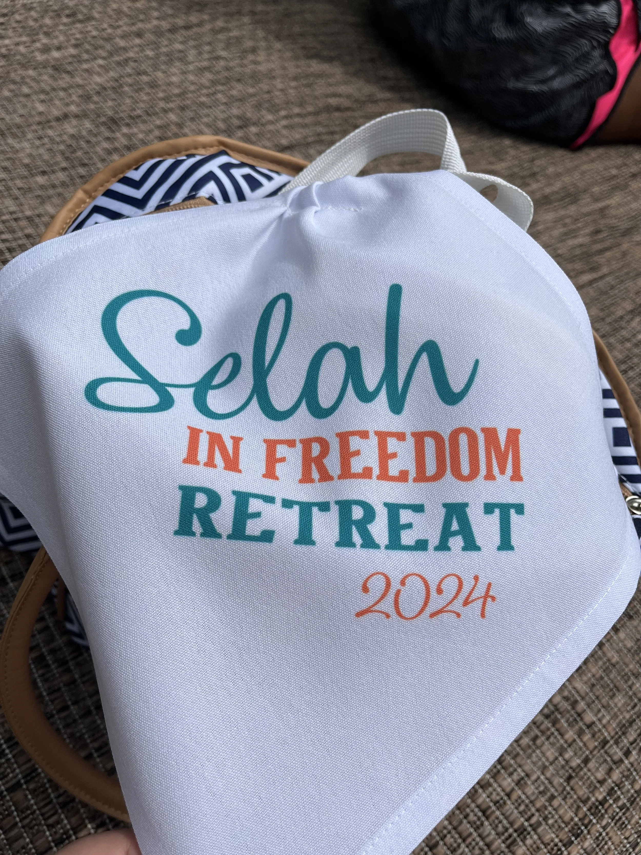 A white bag with colorful text that reads 'Selah In Freedom Retreat 2024' resting on a brown textured surface.