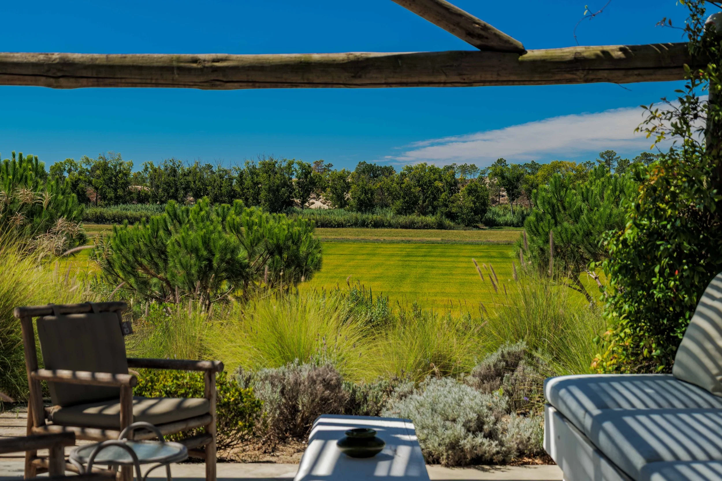 Outdoor patio with chairs and a coffee table overlooking a lush green landscape, blue sky, and trees in the distance.