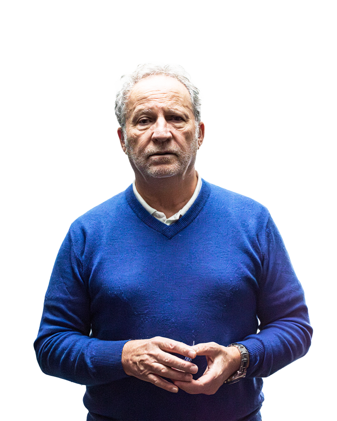 Un homme âgé en pull bleu, avec des cheveux gris, se tient contre un fond blanc, regardant sérieusement.