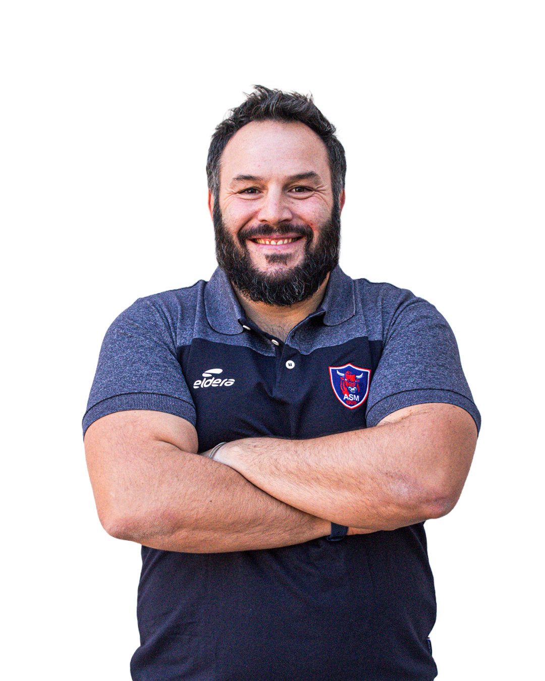 Homme souriant avec une barbe portant un polo bleu avec un logo d'équipe de football, bras croisés.