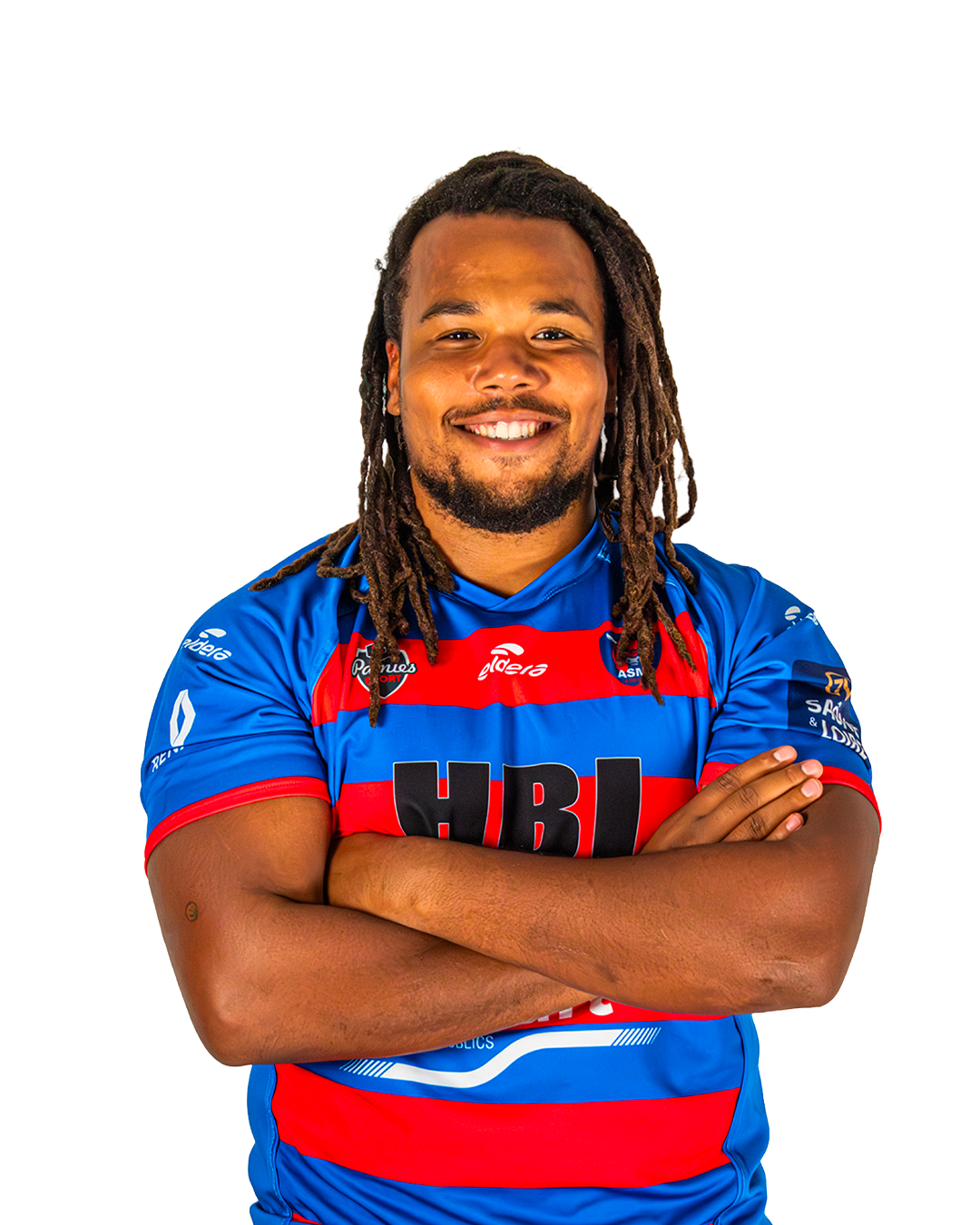 Un homme souriant porte un maillot de rugby bleu avec des bandes rouges, croisant les bras, avec des dreadlocks.