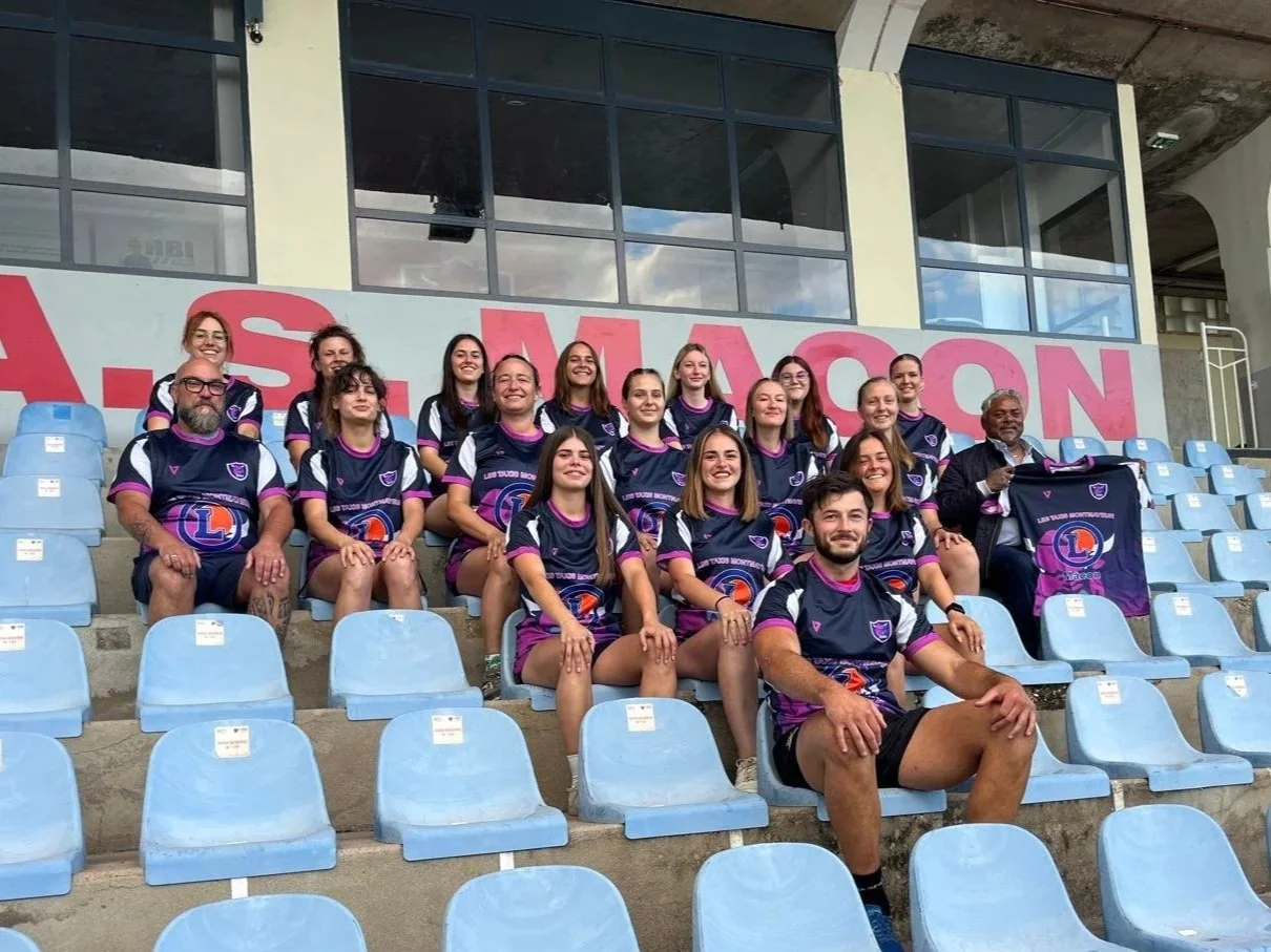 Groupe de jeunes femmes et quelques hommes portant des maillots de sport violets et noirs, assis dans les tribunes d'une tribune de stade, posant pour la photo.