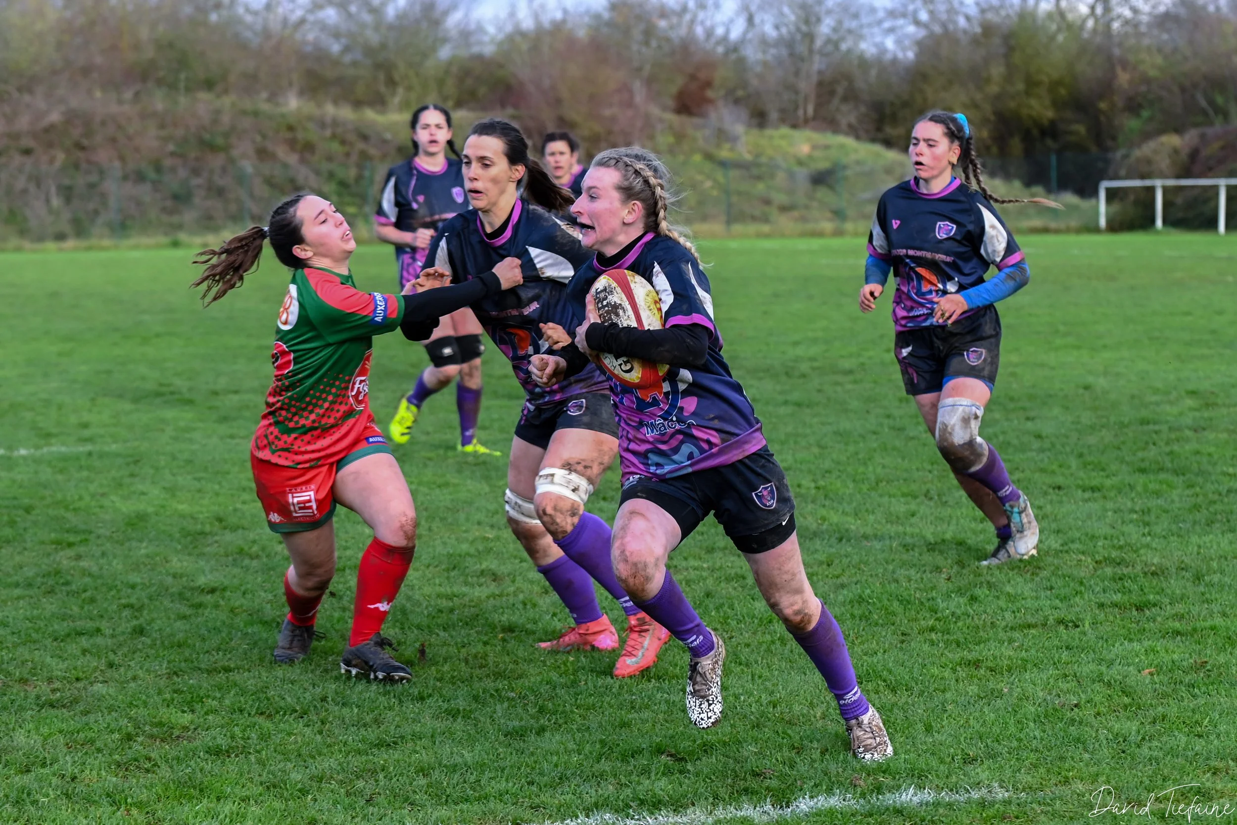 Femmes jouant au rugby sur un terrain herbeux, combat intense pour le ballon avec plusieurs joueuses impliquées.