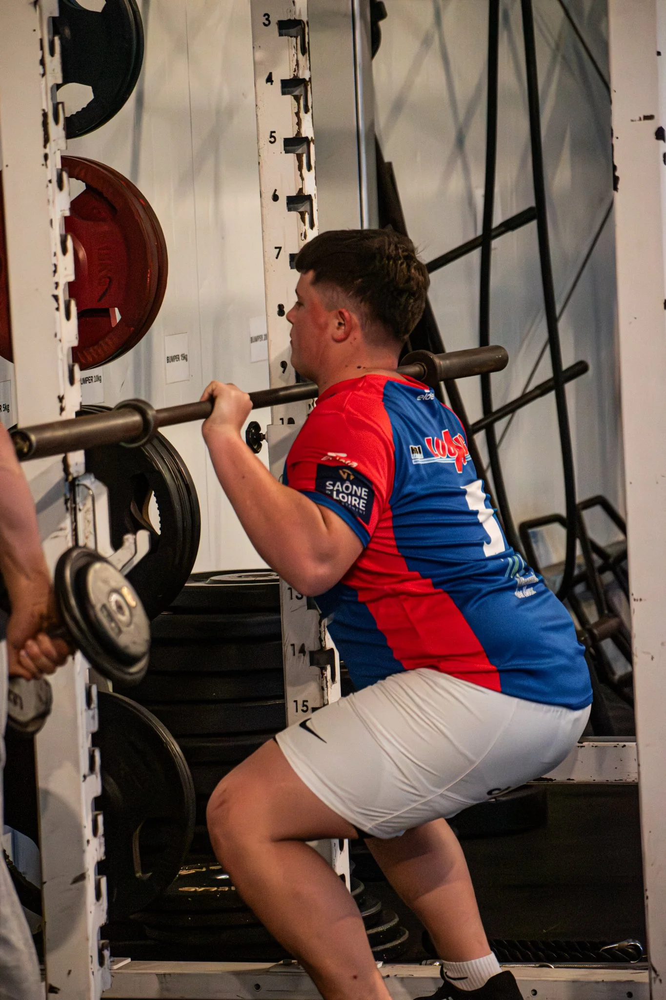 Un homme en train de faire des squats avec une barre en musculation dans une salle de sport.