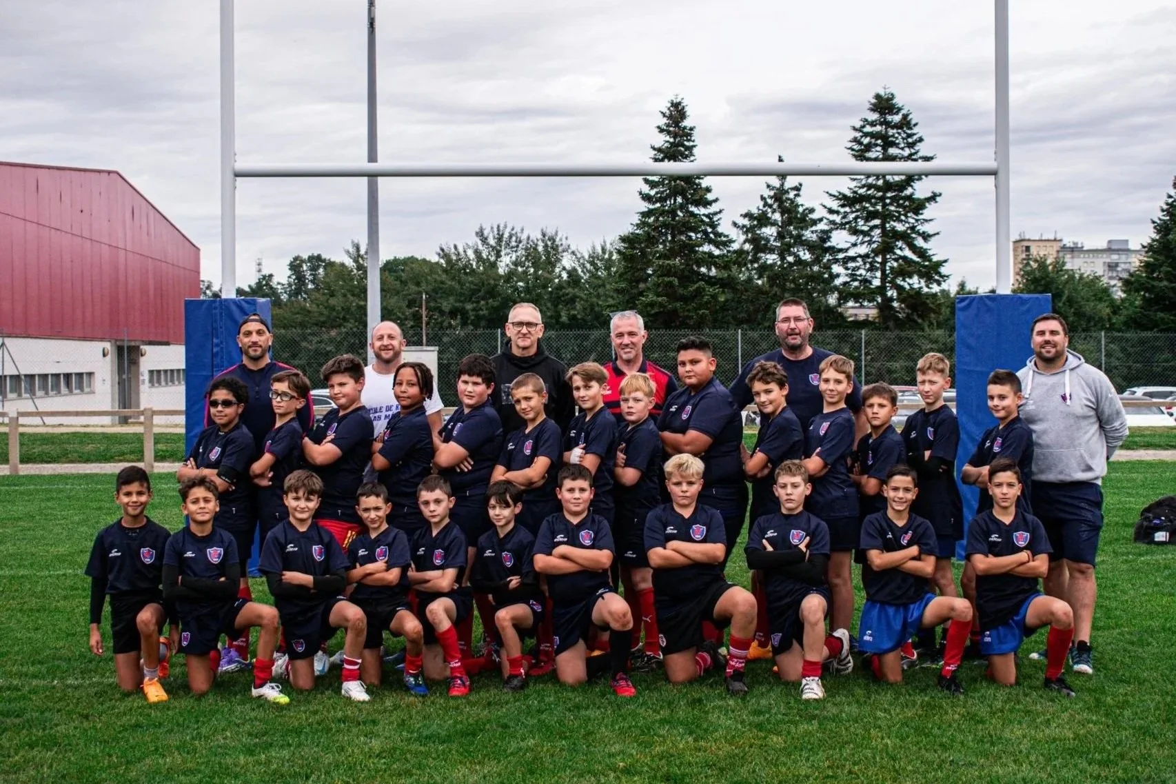 Groupe de jeunes joueurs de rugby et leurs entraîneurs posant pour une photo sur un terrain de rugby