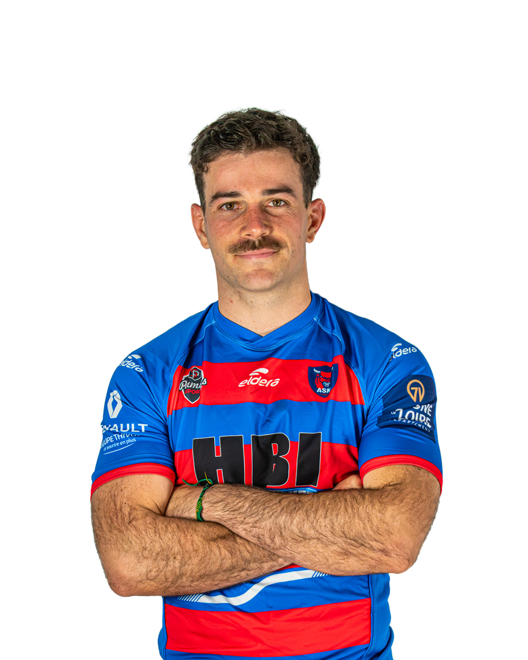 Un homme en maillot de rugby bleu avec des rayures rouges, portant un bracelet vert, les bras croisés, face à la caméra.