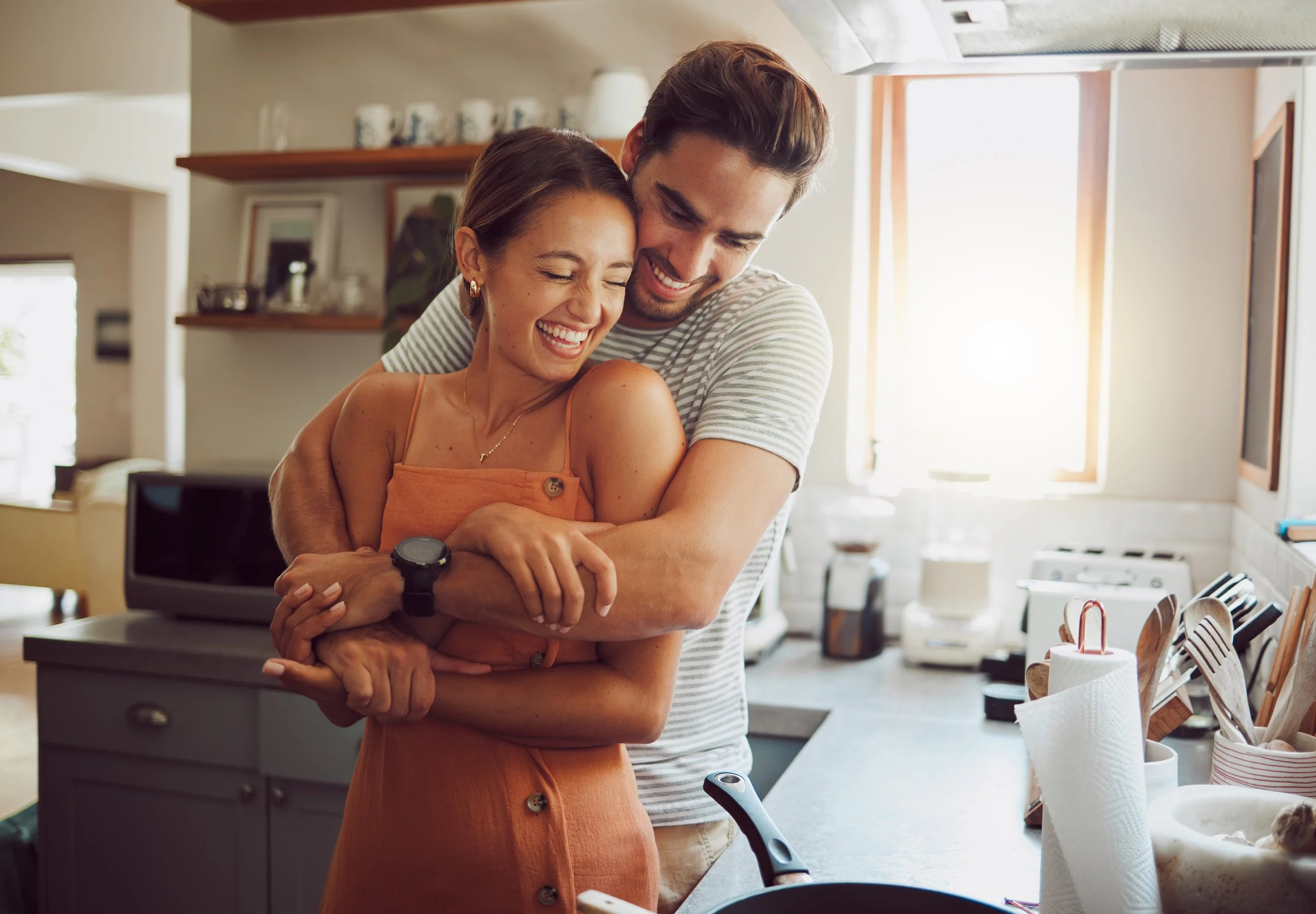 A happy couple hugging in a kitchen, both smiling and laughing warmly.