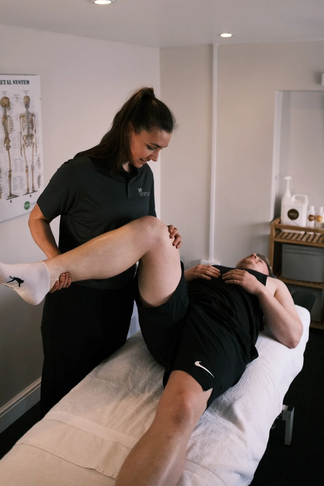 A physical therapist assists a person with a leg stretch exercise on a treatment table in a therapy room.