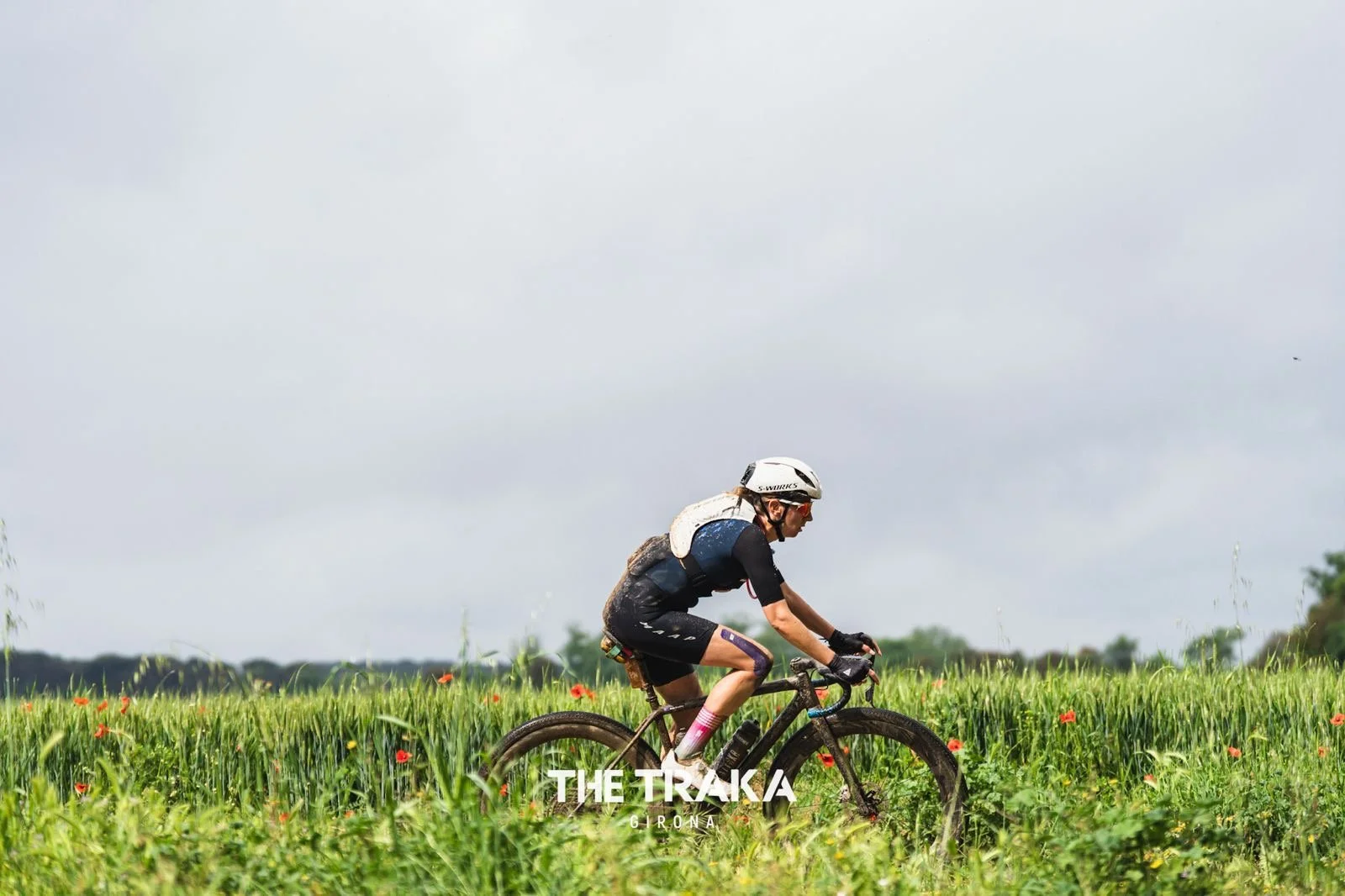 A person riding a mountain bike through a grassy field on a cloudy day.