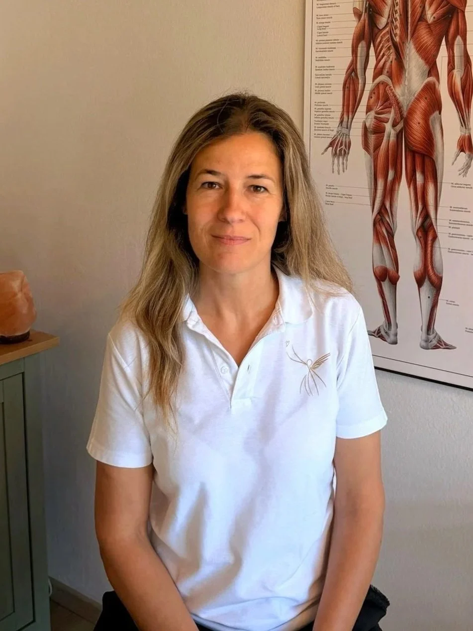 Cristina Gabor seduta in  nel suo ufficio nel Centro Terapeutico Gambarogno con un poster anatomico del corpo umano sullo sfondo.