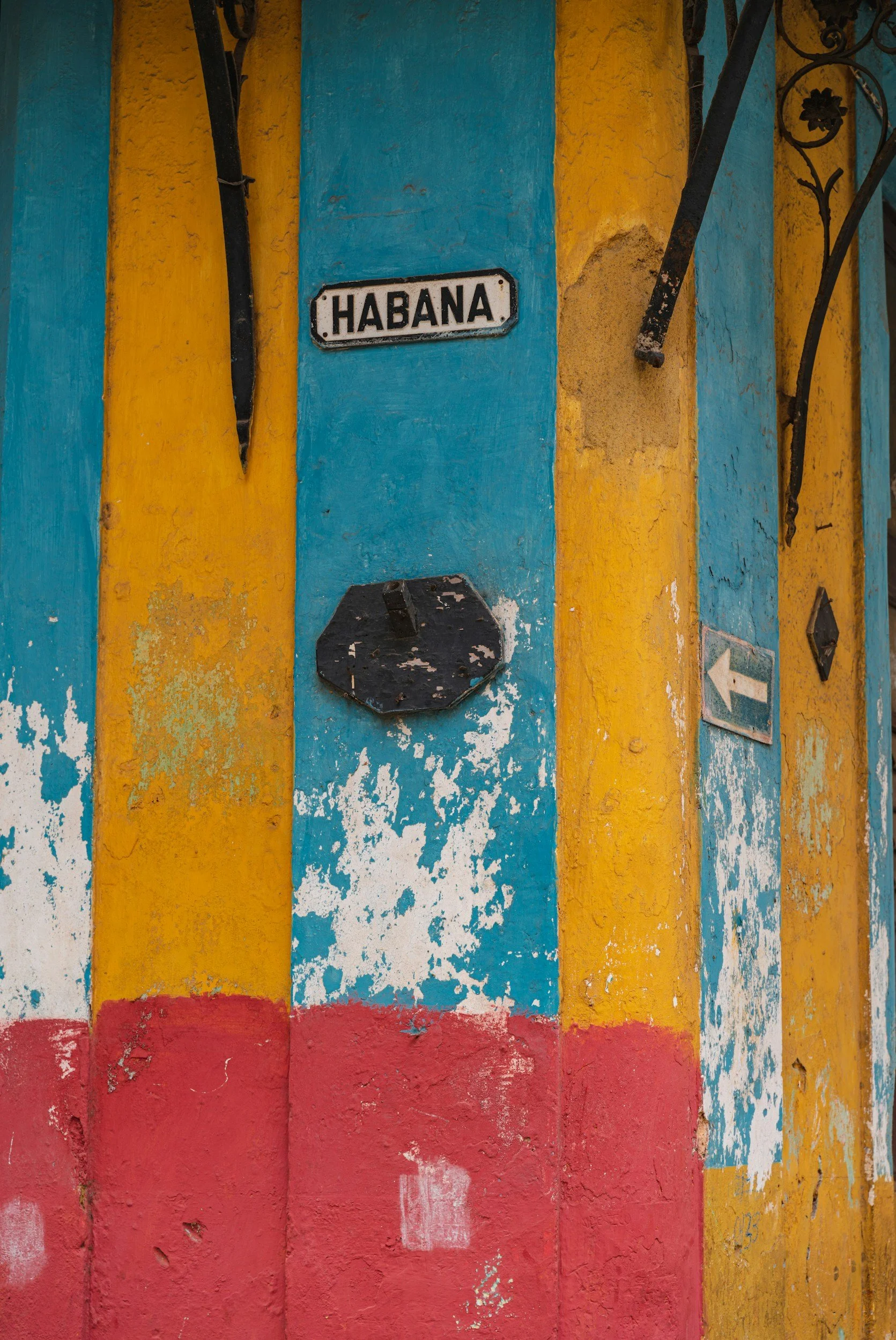 Pared con colores azul, amarillo y rojo con señales de tránsito, incluyendo una placa que dice 'Habana' y una flecha blanca apuntando a la izquierda.
