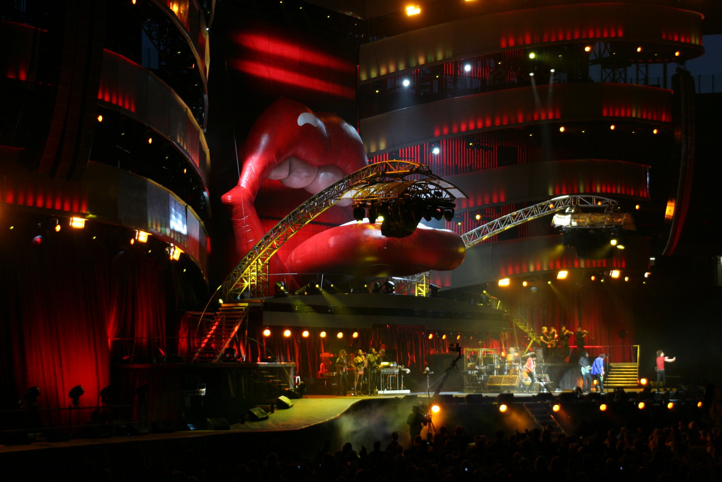 Bühne auf einem Konzert mit einem großen roten Lippen-Design im Hintergrund, Bühnenbeleuchtung und Musikern, die auftreten.