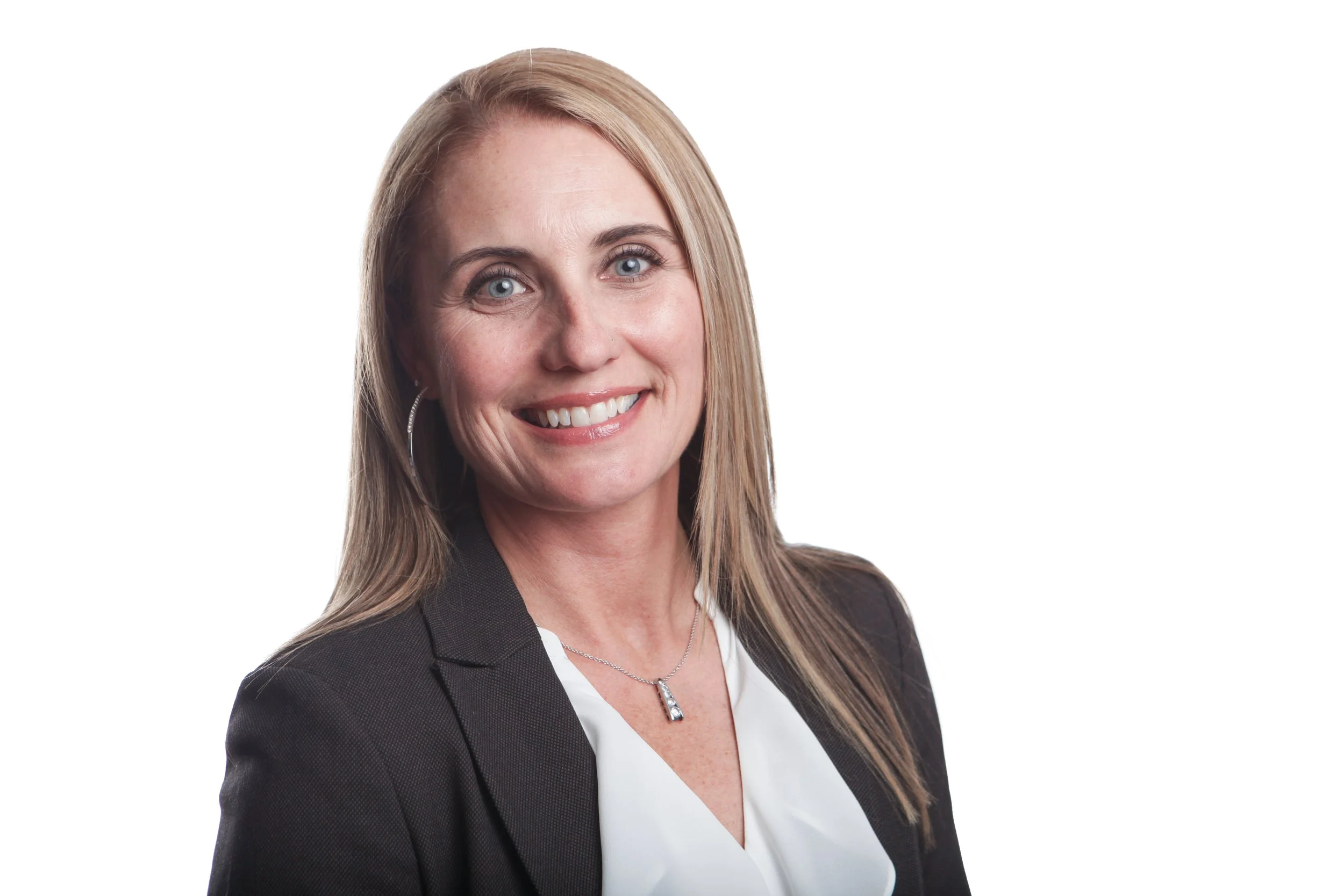 A woman with long blonde hair, blue eyes, and a friendly smile, wearing a black blazer, white blouse, earrings, and a necklace, against a white background.