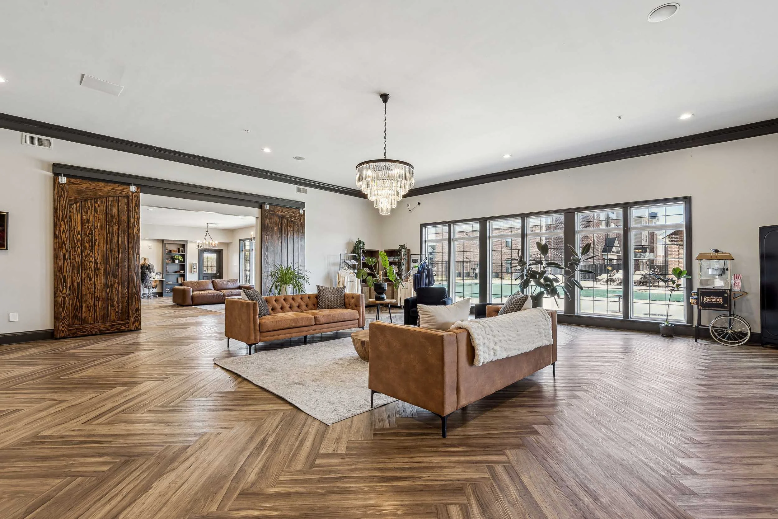 Spacious resident lounge with large windows, wooden flooring, modern chandelier, and comfortable seating.
