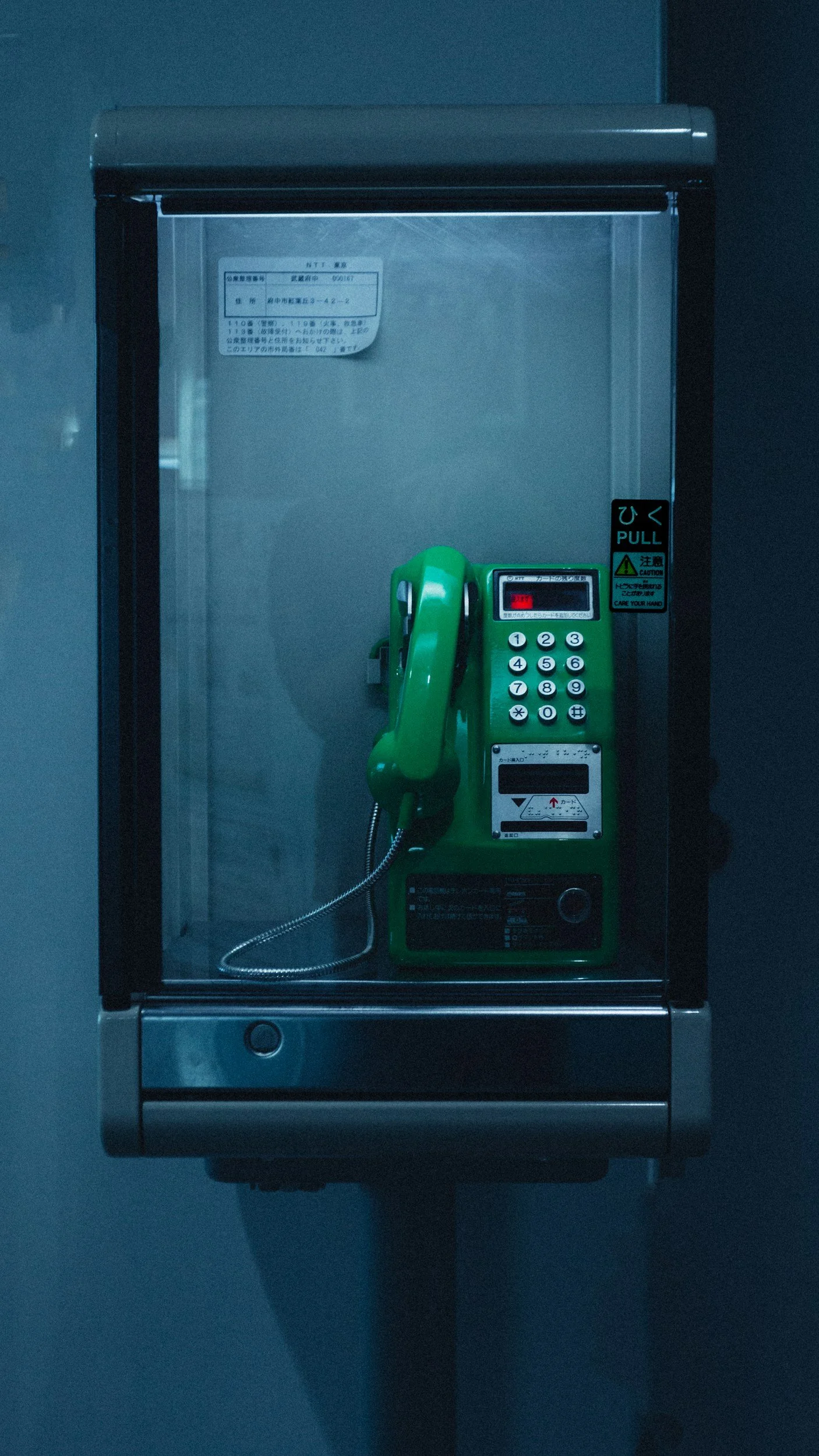 A green payphone enclosed in a glass case mounted on a wall.