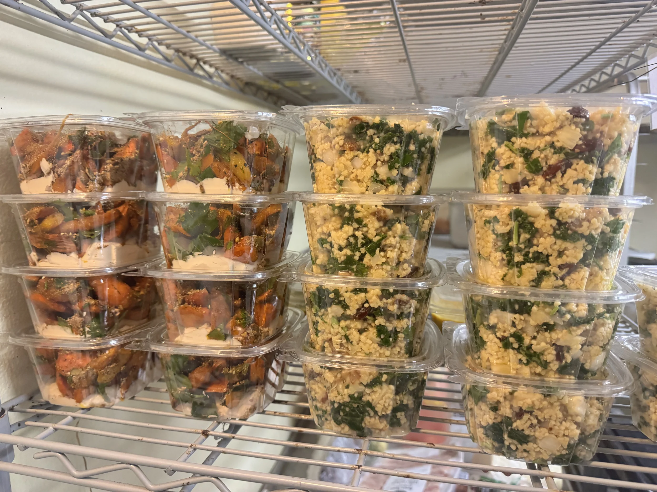 Pre-packaged salads in clear plastic containers on a metal shelf, including chopped vegetables and greens.