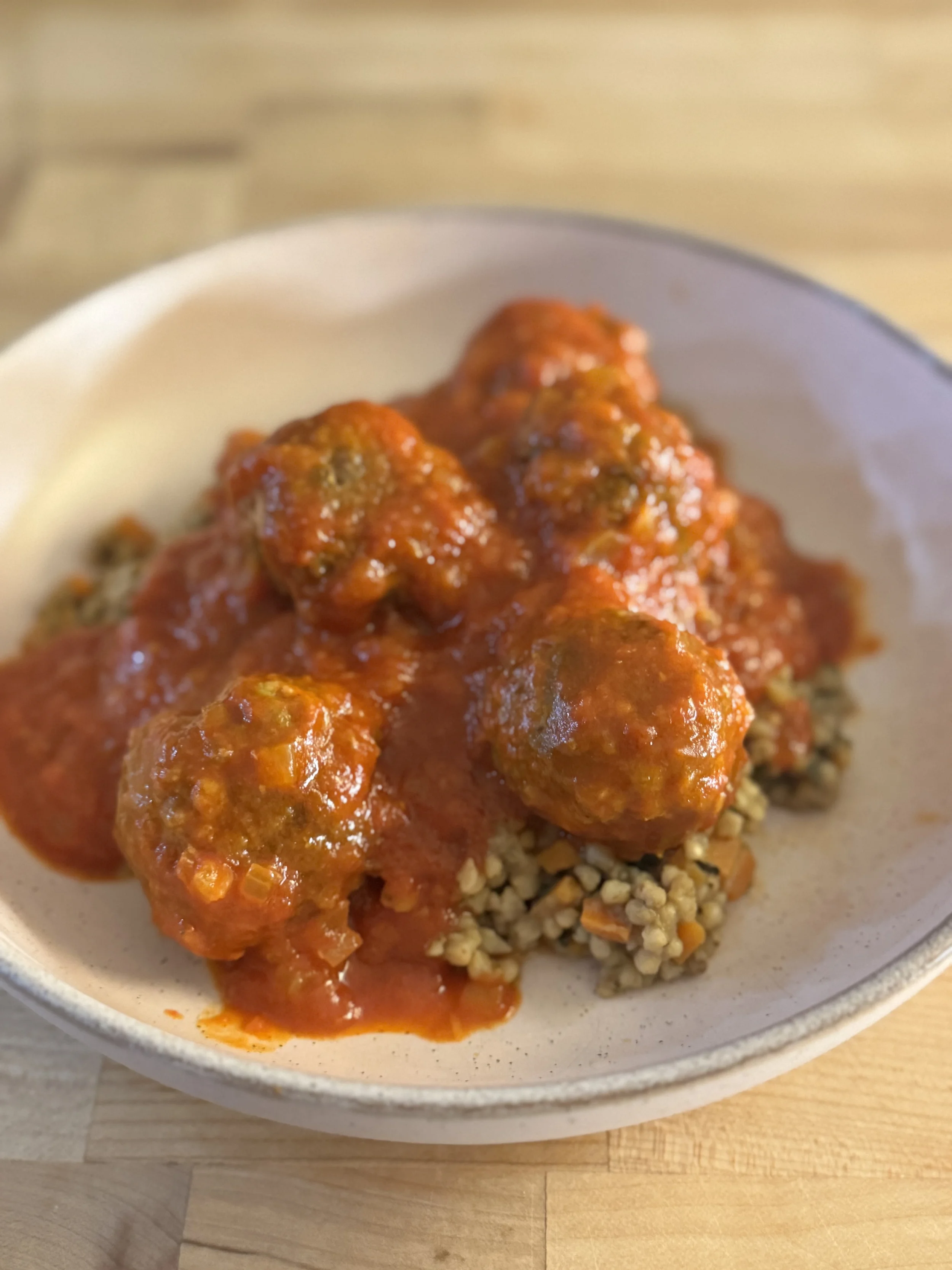 Plate of cooked meatballs in tomato sauce served over grain, on a round white plate.