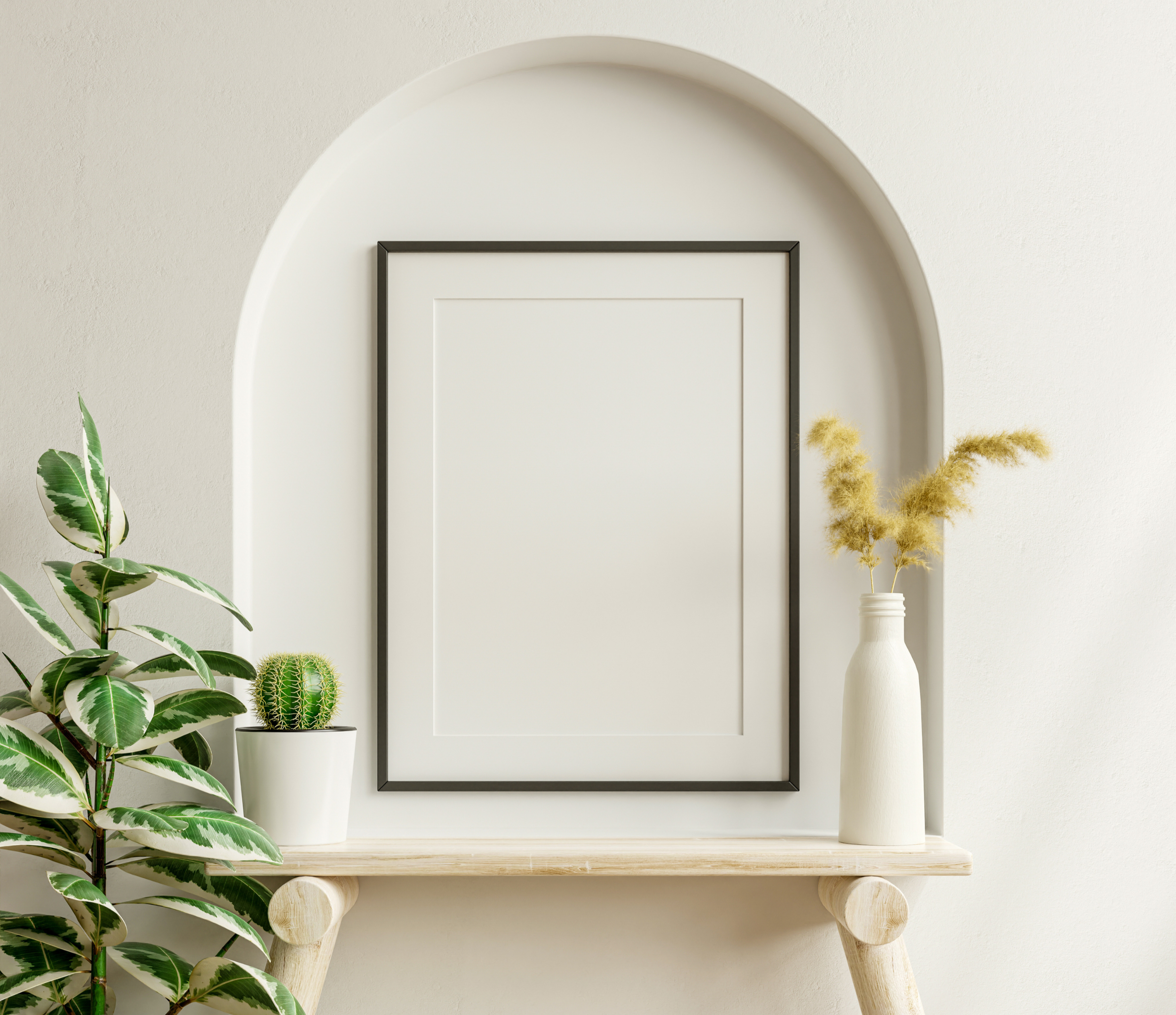 Decorative interior scene with a framed blank white poster, green potted cactus, and yellow pampas grass in white vases on a wooden shelf against a white wall with an arched niche.