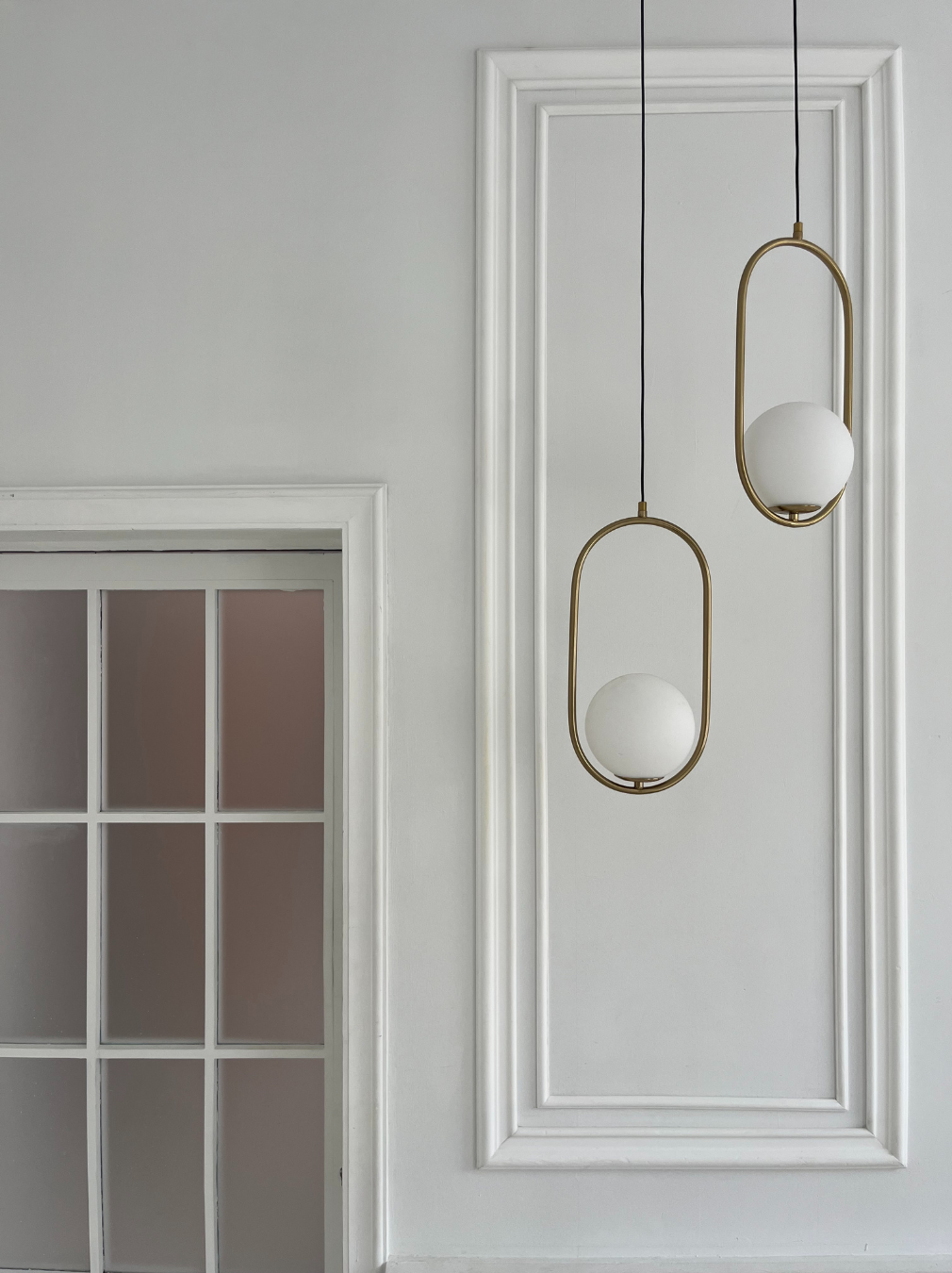 Interior wall with two modern hanging pendant lights with white spherical globes and brushed gold framing, next to a door with multiple glass panes.
