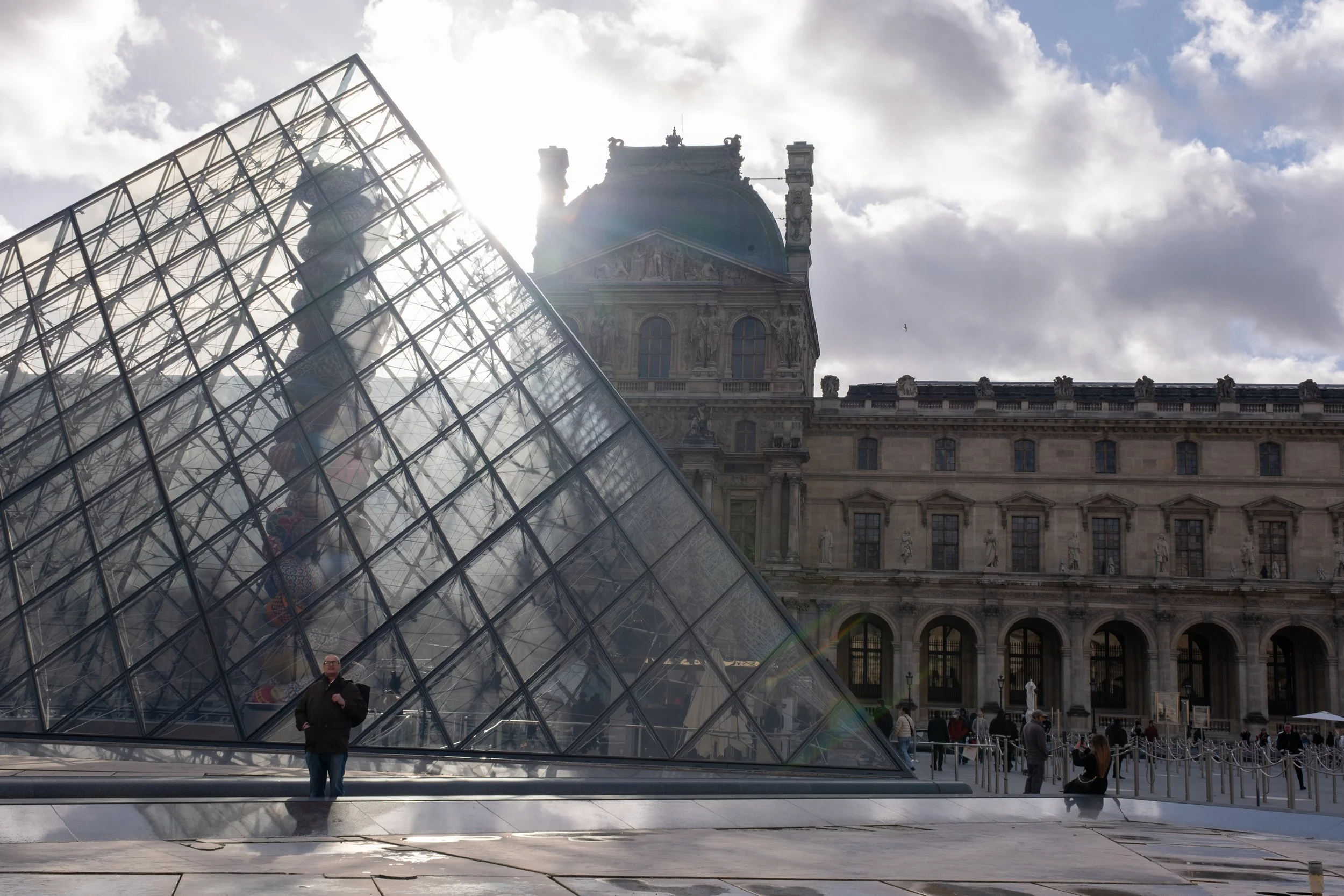 Man in a sunbeam beneath the pyramid entry of the Louvre Museum, Paris, France.
