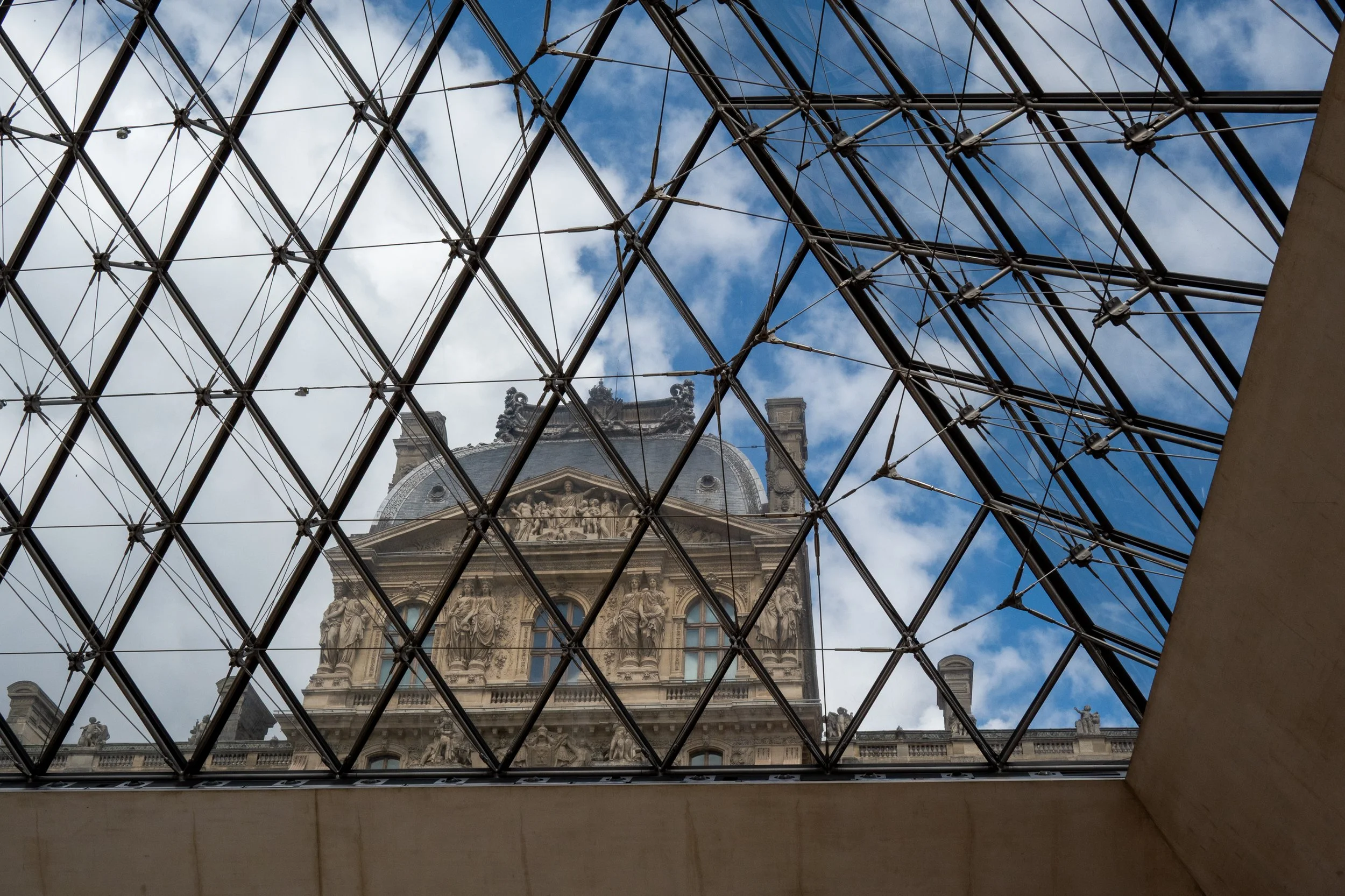 View of a historic ornate building through the glass roof of the Louvre Museum in Paris, France.