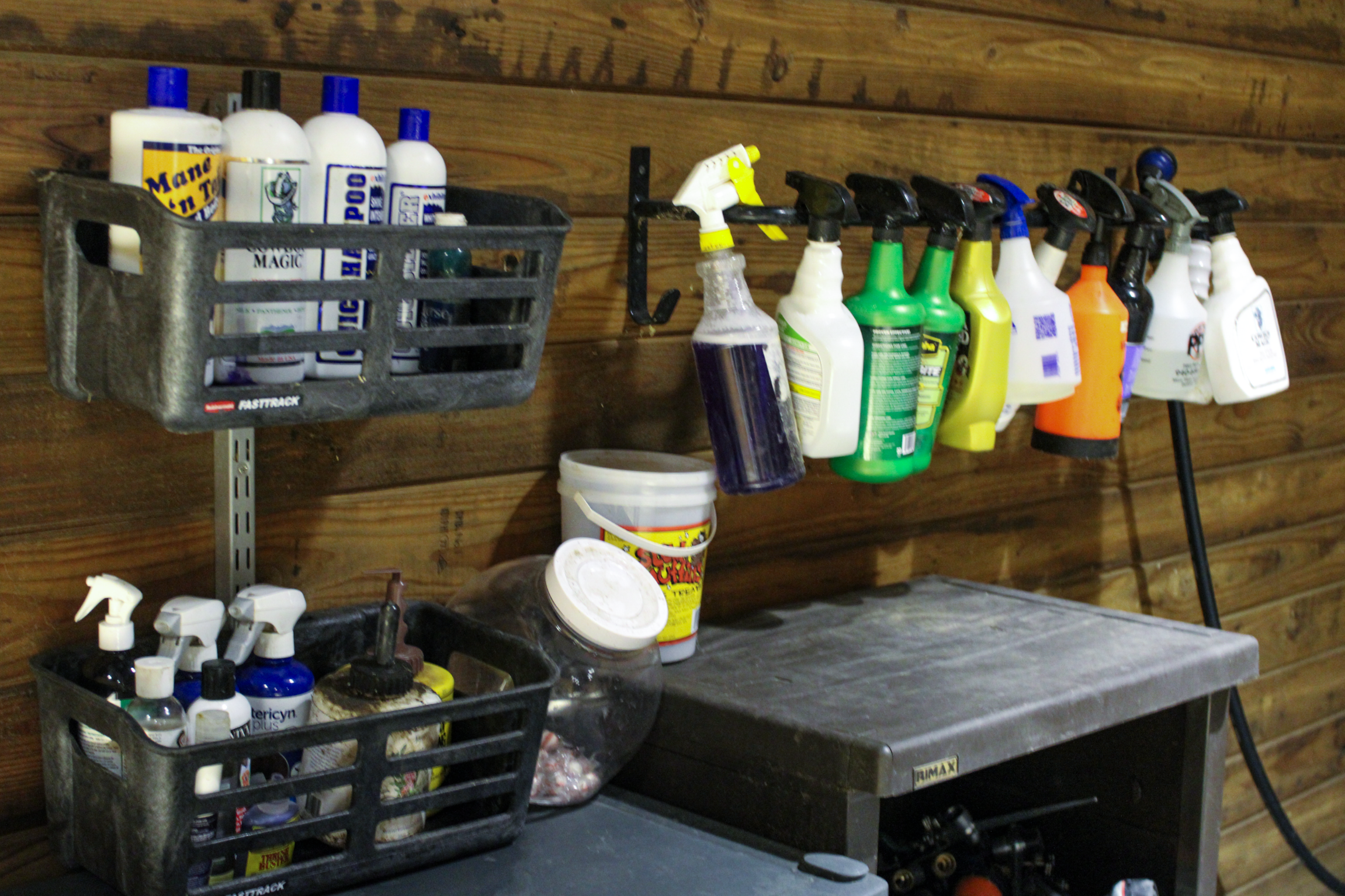 Shelves and containers with cleaning supplies, spray bottles, and tools against a wooden wall.