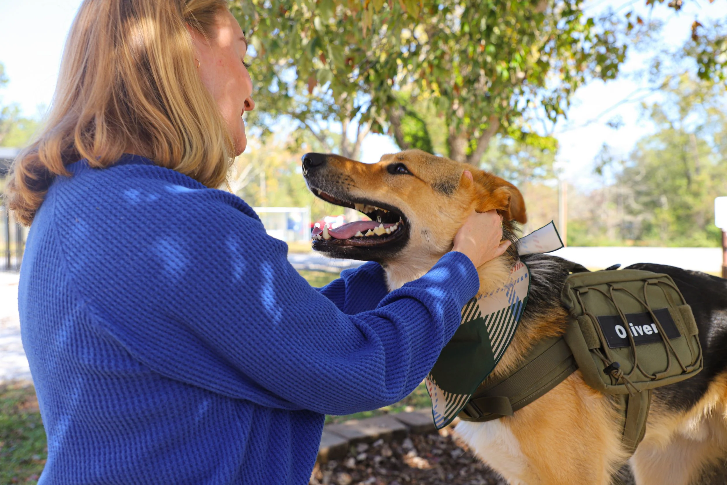 Woman in a blue jacket holding and smiling at a service dog outdoors
