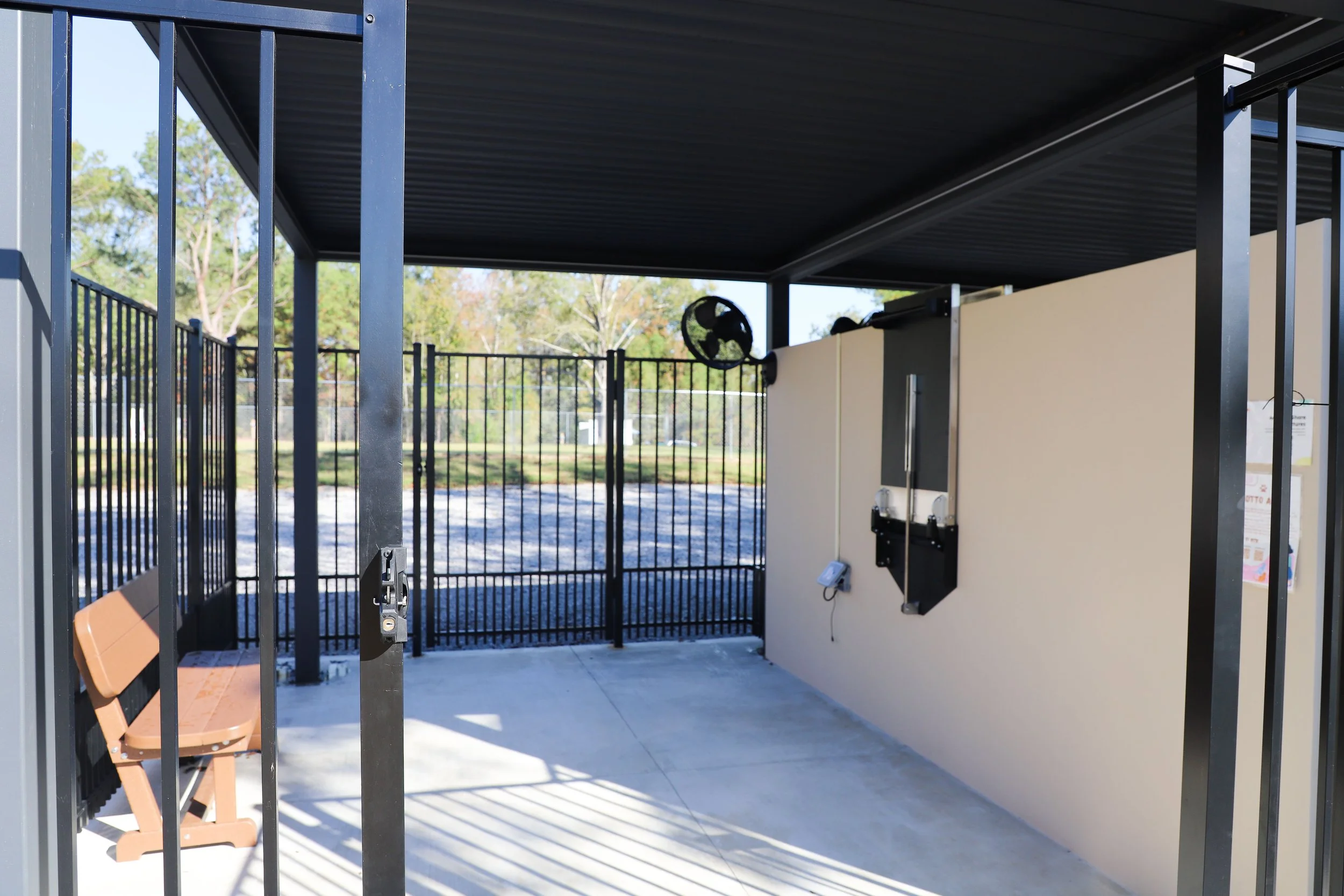 Empty dog agility training shelter with a brown bench and fenced outdoor area in the background.