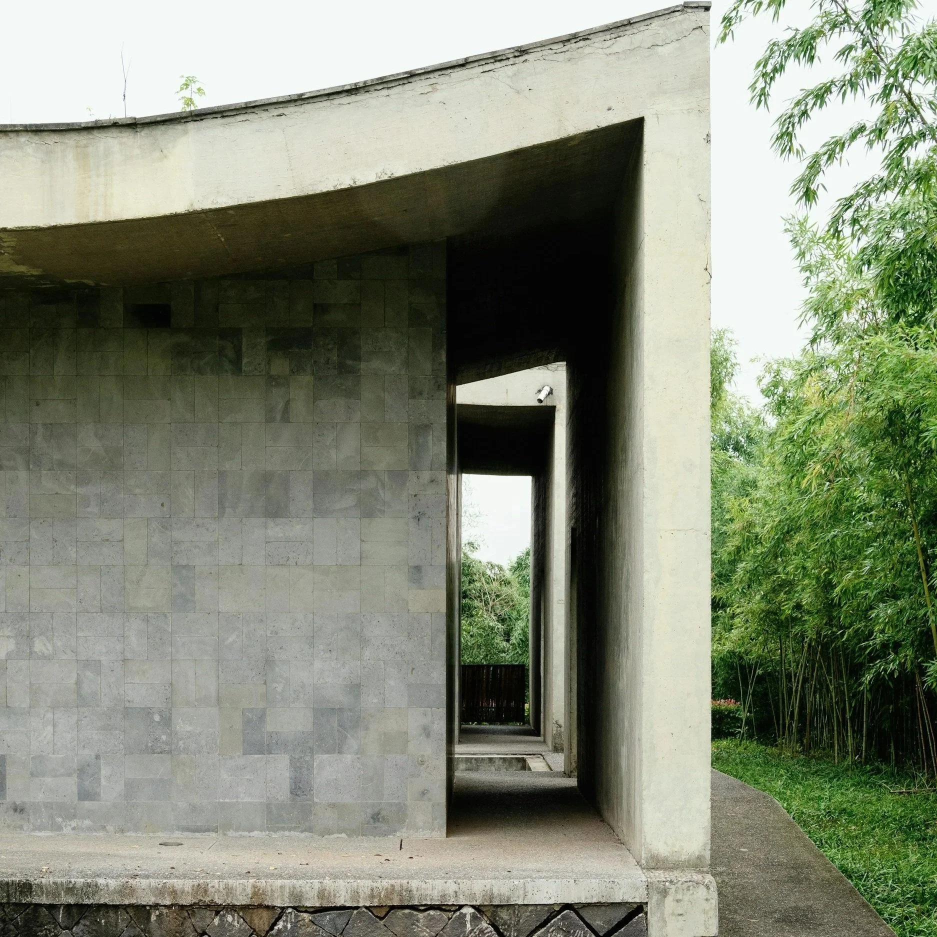 Concrete building with an open corridor and a large square opening, surrounded by greenery.