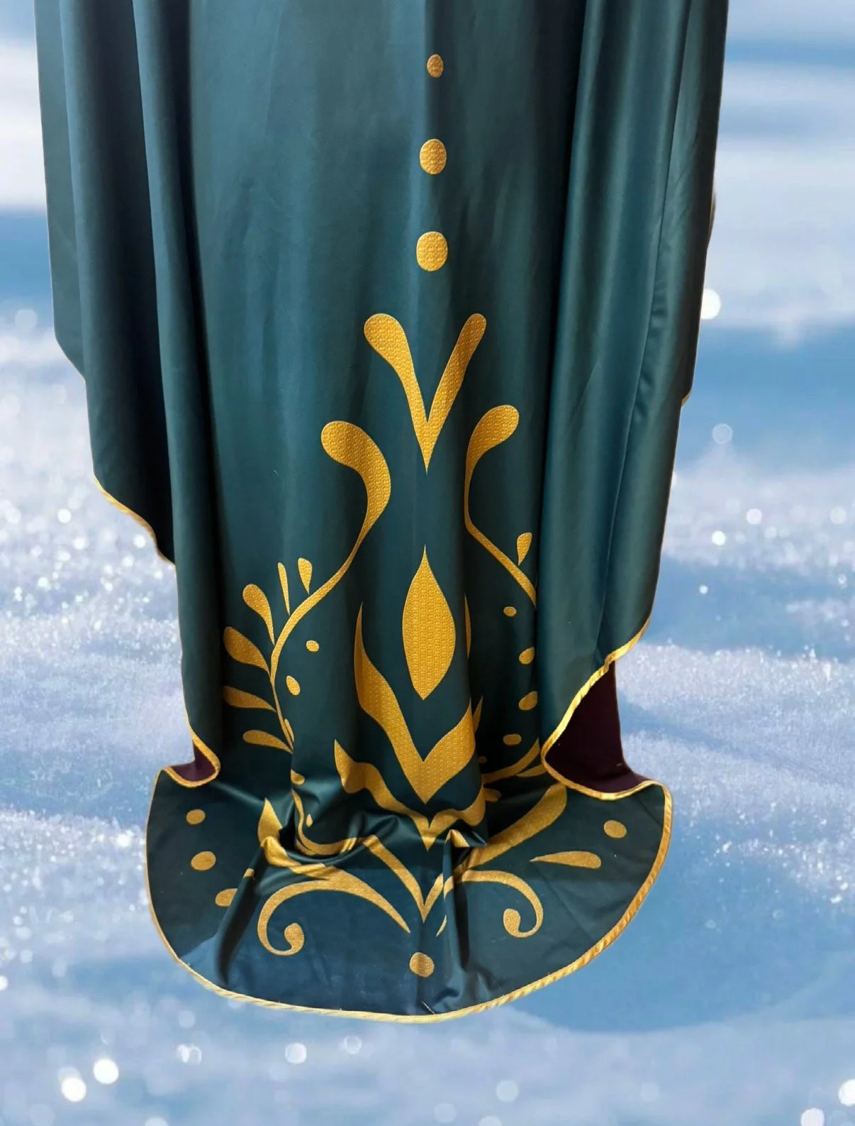 Close-up of a green fabric with gold decorative patterns hanging over snow and ice.