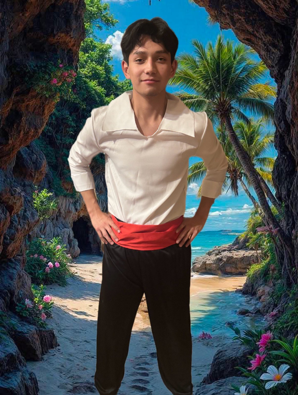 Young man with dark hair, white shirt, red sash, and black pants standing with hands on hips on a beach surrounded by tropical rocks and palm trees.