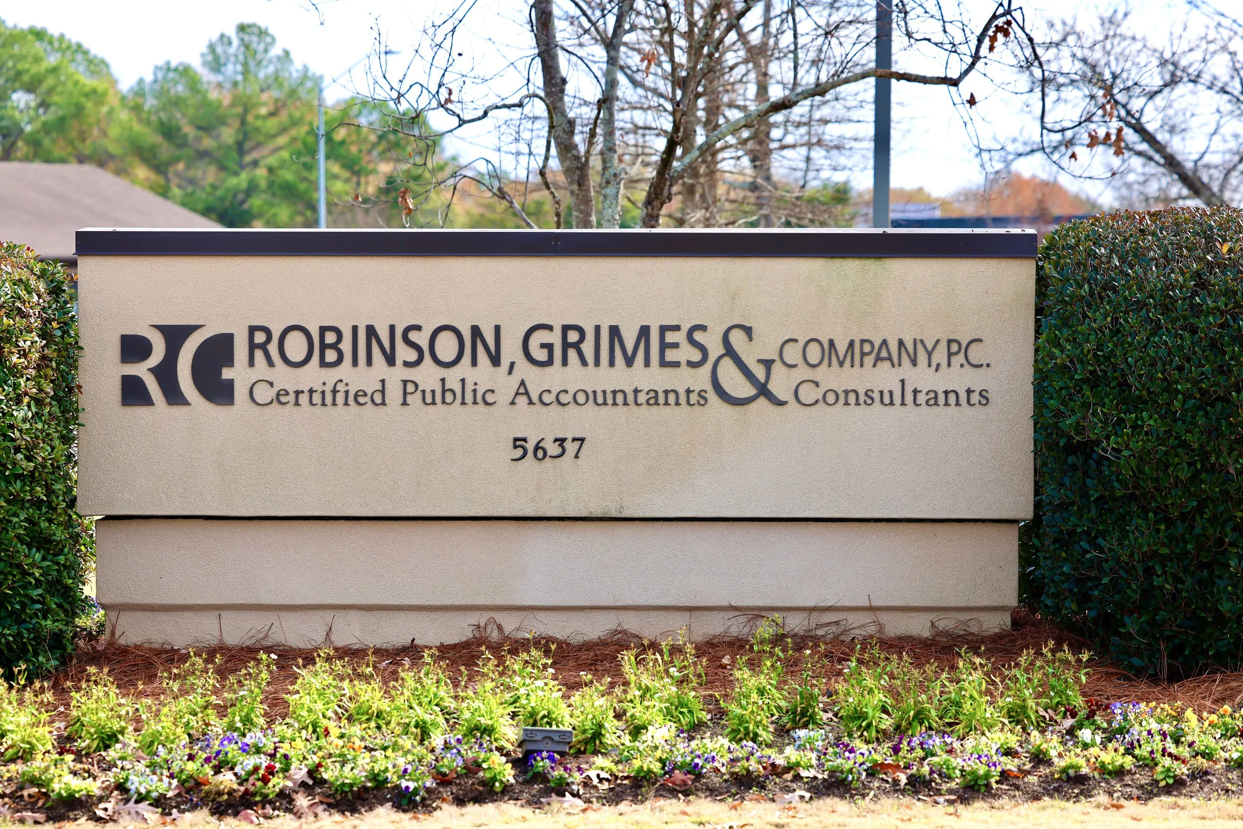 Sign for Robinson, Grimes & Company, P.C., Certified Public Accountants and Consultants, with the address 5637, surrounded by shrubs and flowers, in a suburban setting.