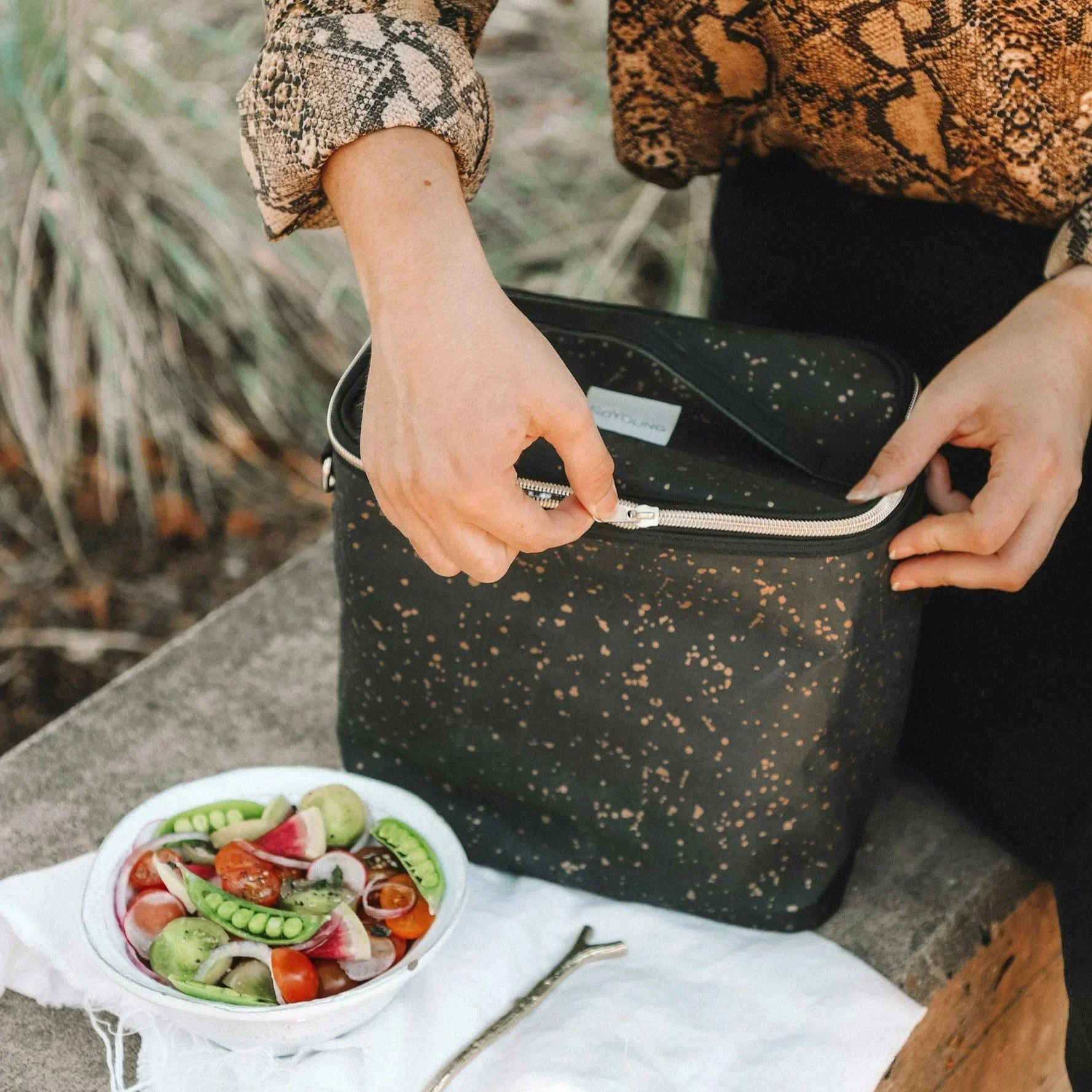 girl's arms closing a lunchbox next to a salad on a table