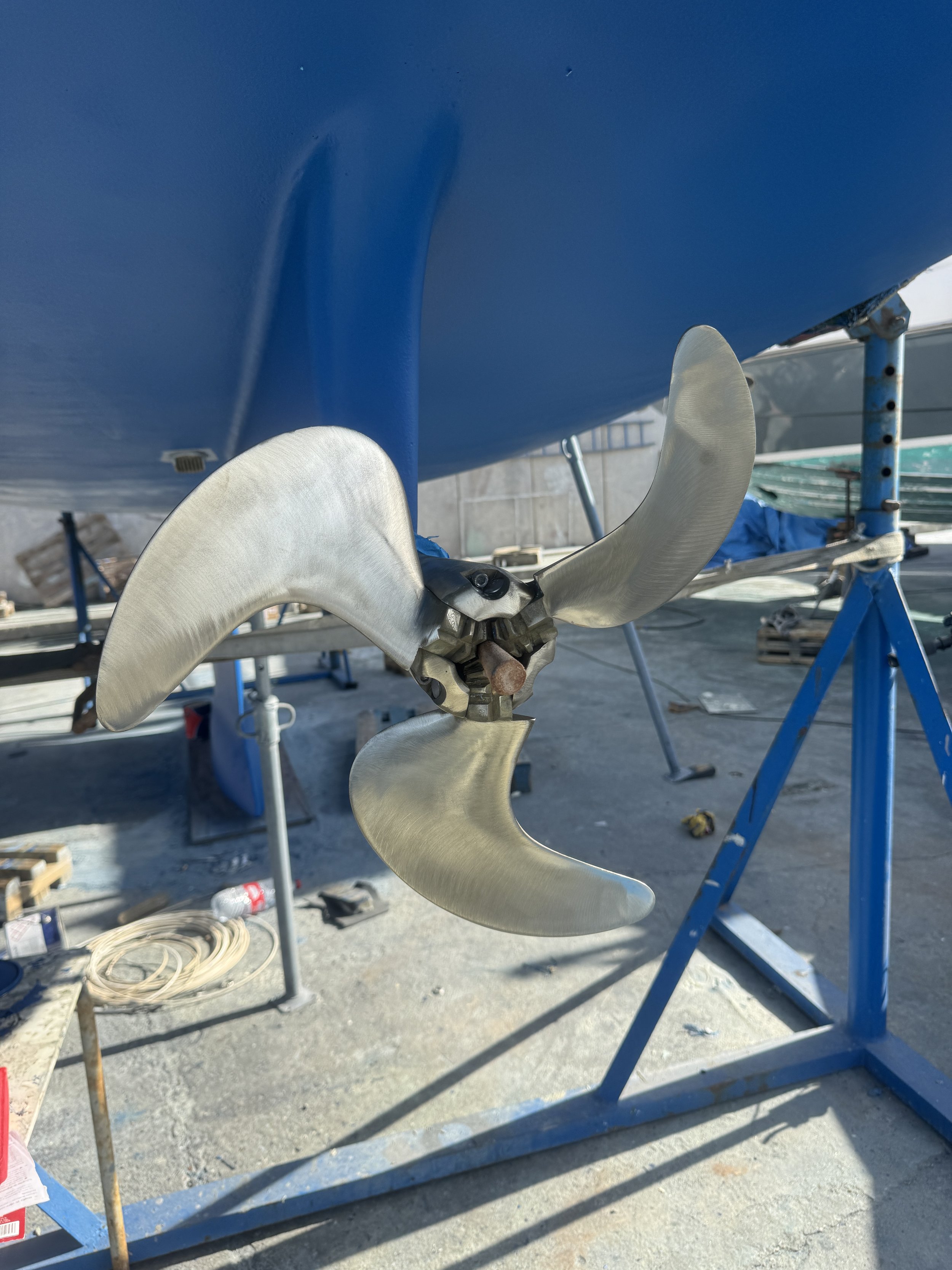 Close-up of a boat propeller with four blades mounted on a boat underneath a blue hull in a boatyard. helices propeller montar y reparar, pintar, nauticampello