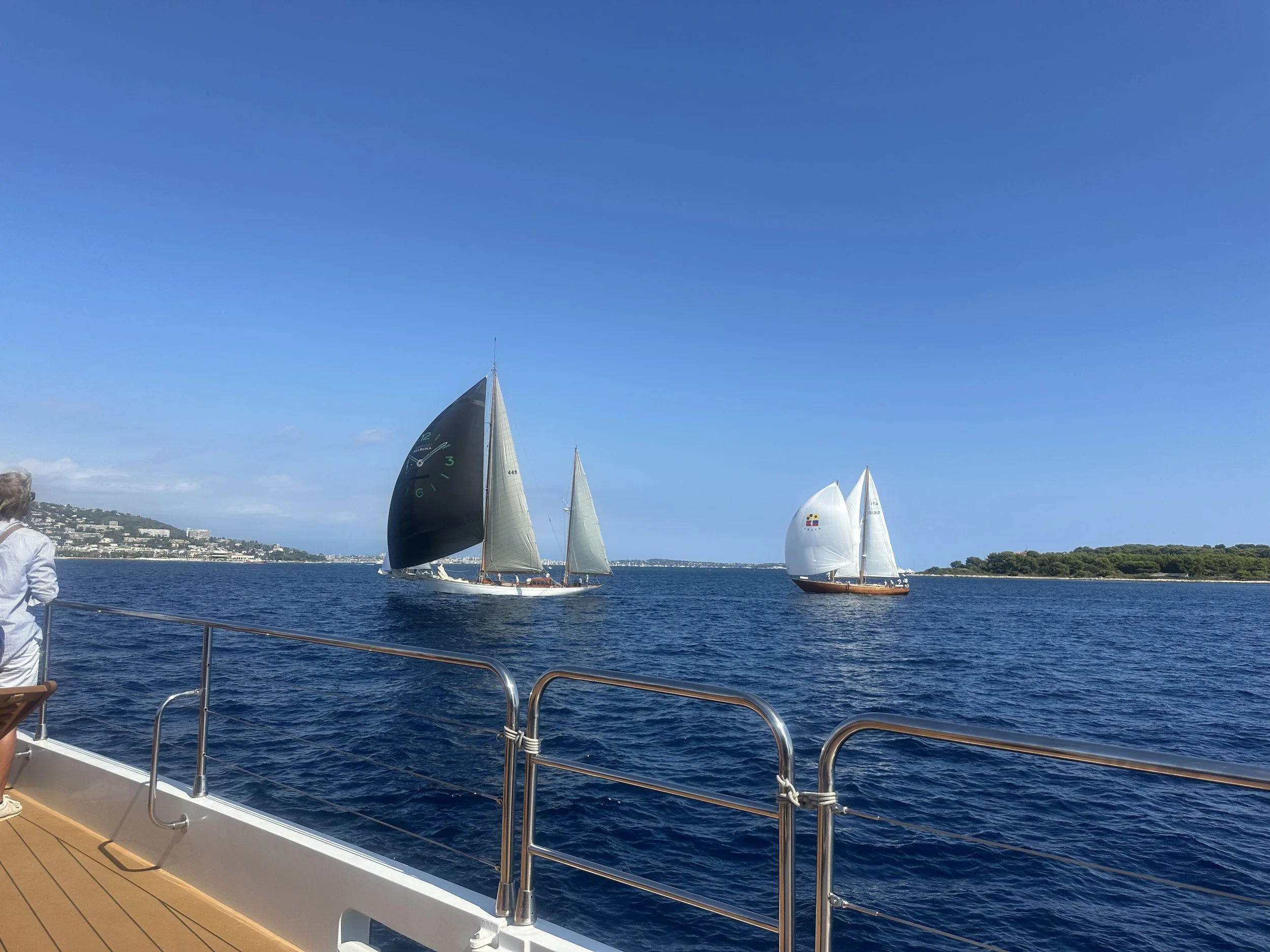 View from a catamaran deck of two classic yachts with spinnakers racing near the Lérins Islands off Cannes