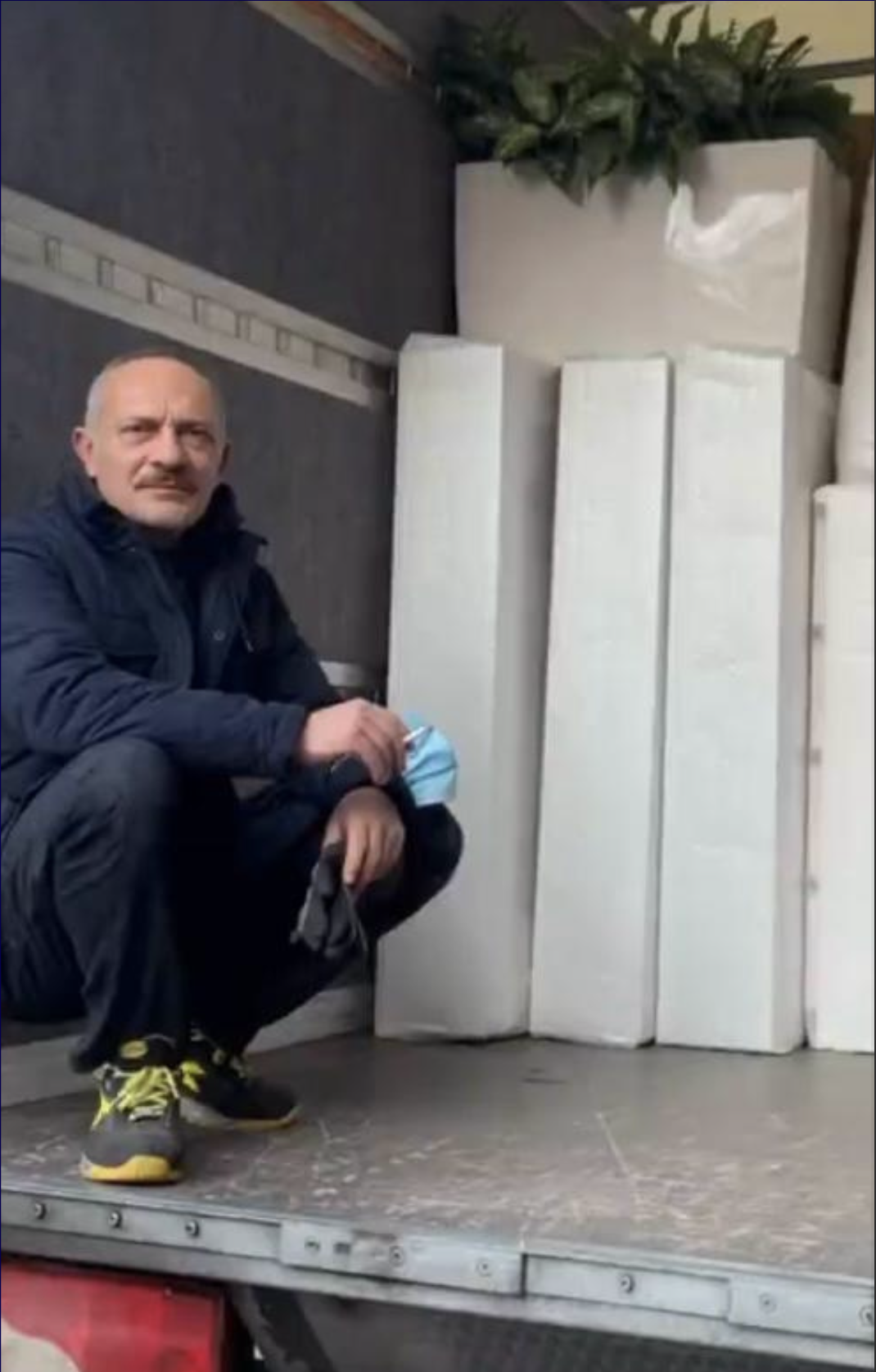 Uomo in ginocchio su una piattaforma, con sfondo piante e oggetti bianco