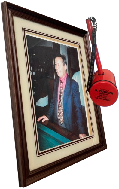 Foto di un uomo in abito elegante in cornice, accompagnata da un telefono d'emergenza rosso appeso alla cornice stessa.