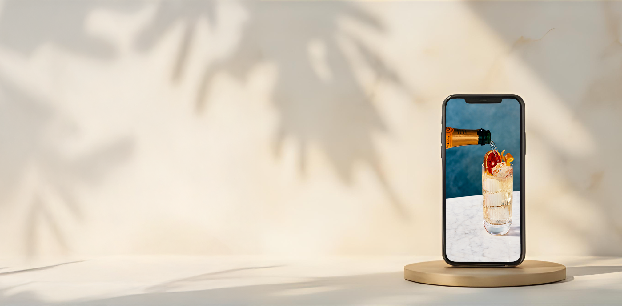 A smartphone on a stand displays a photo of an elegant champagne cocktail with grapefruit garnish, representing luxury and ambiance.