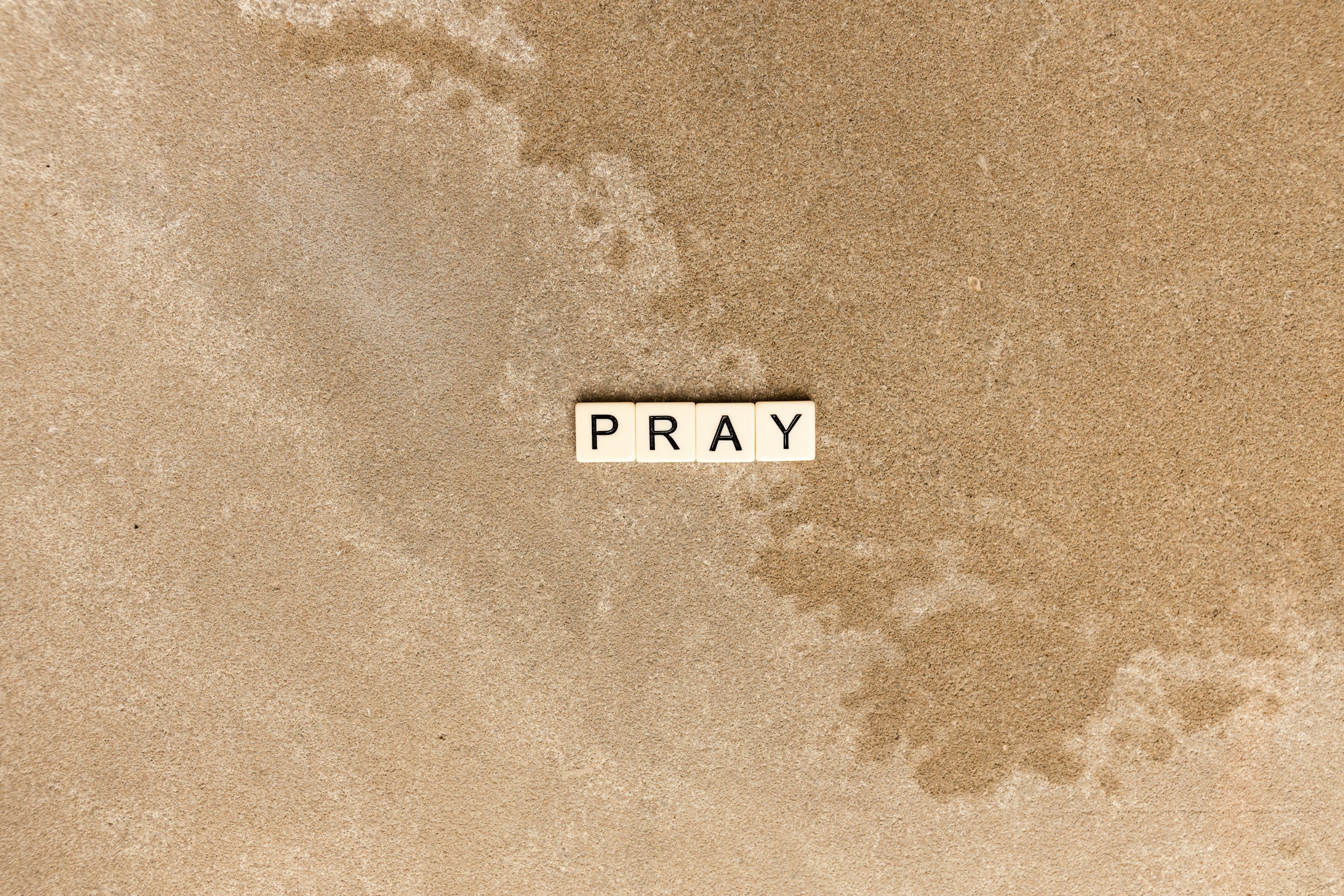 Letter tiles spelling out 'PRAY' on the sand at the beach