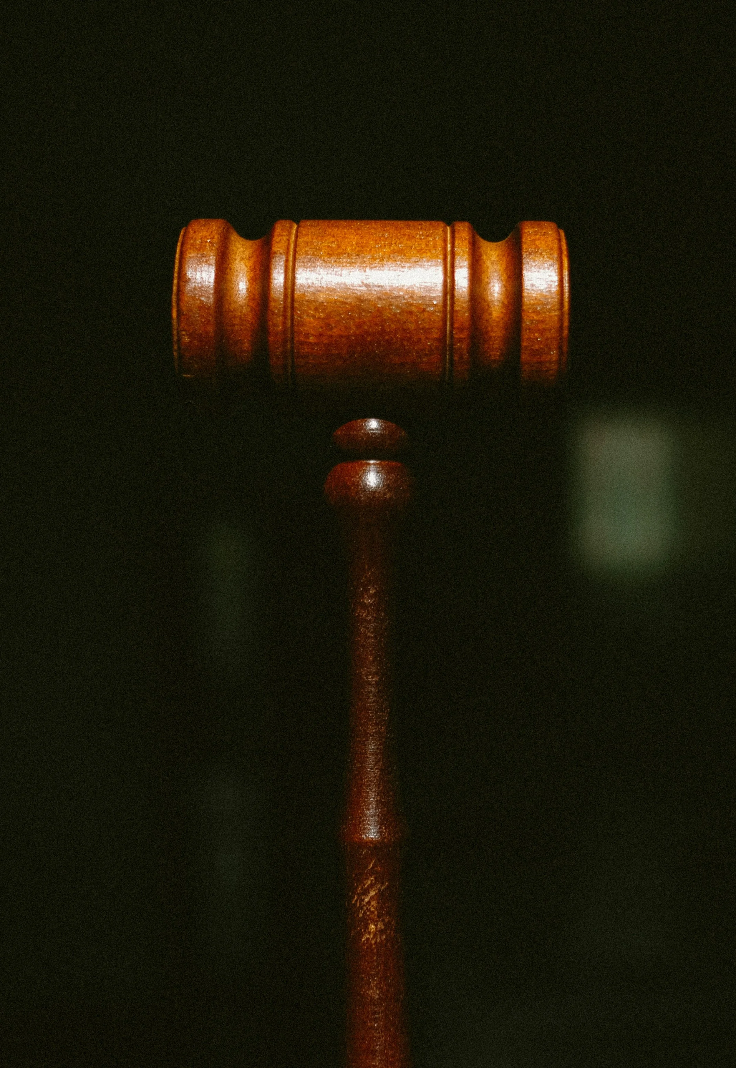 A wooden judge's gavel laying horizontally on a dark surface with a small wooden sound block below it.