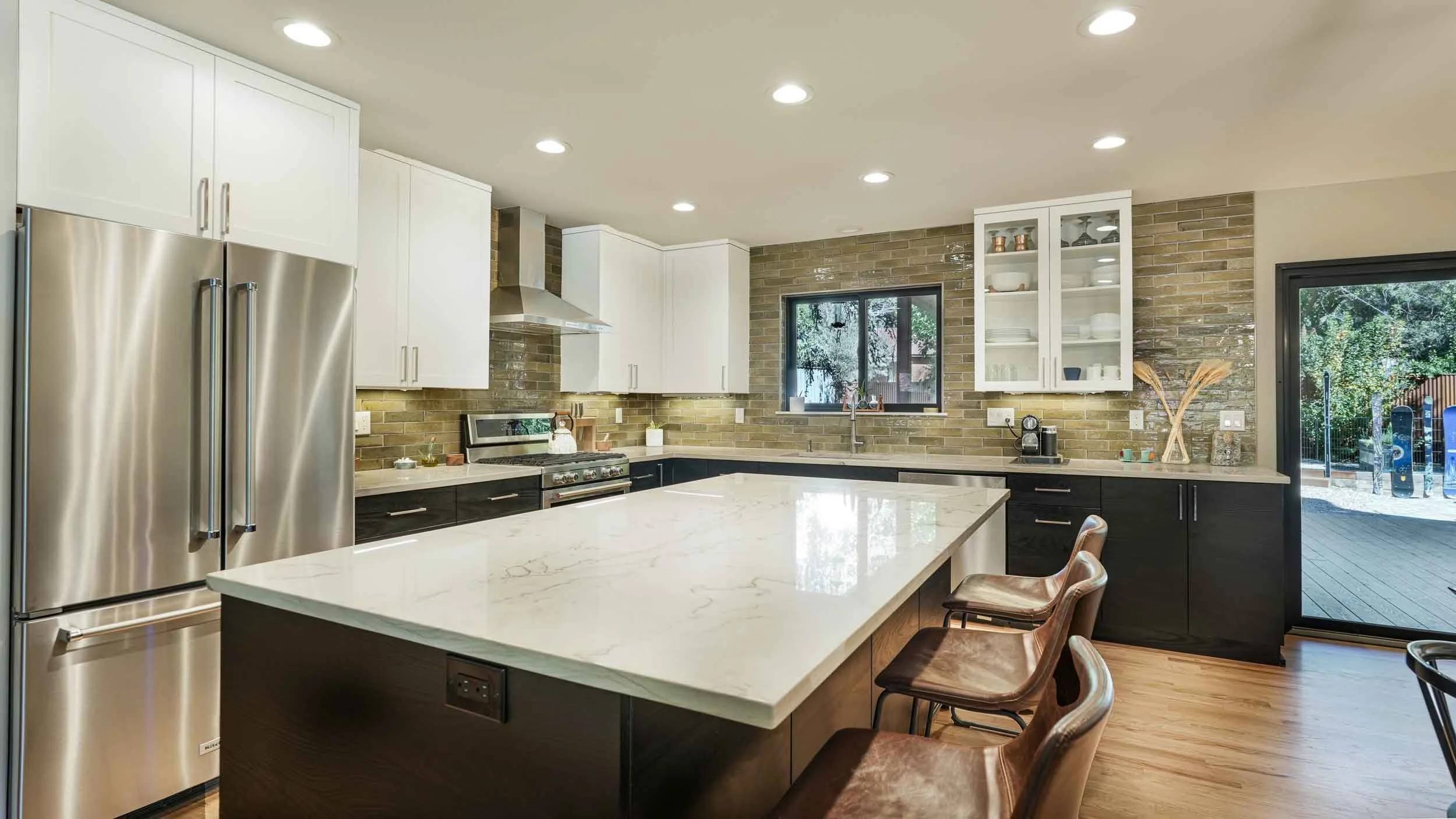Modern kitchen with white upper cabinets, black lower cabinets, a large island with a marble countertop, stainless steel refrigerator built by home builders in durango colorado